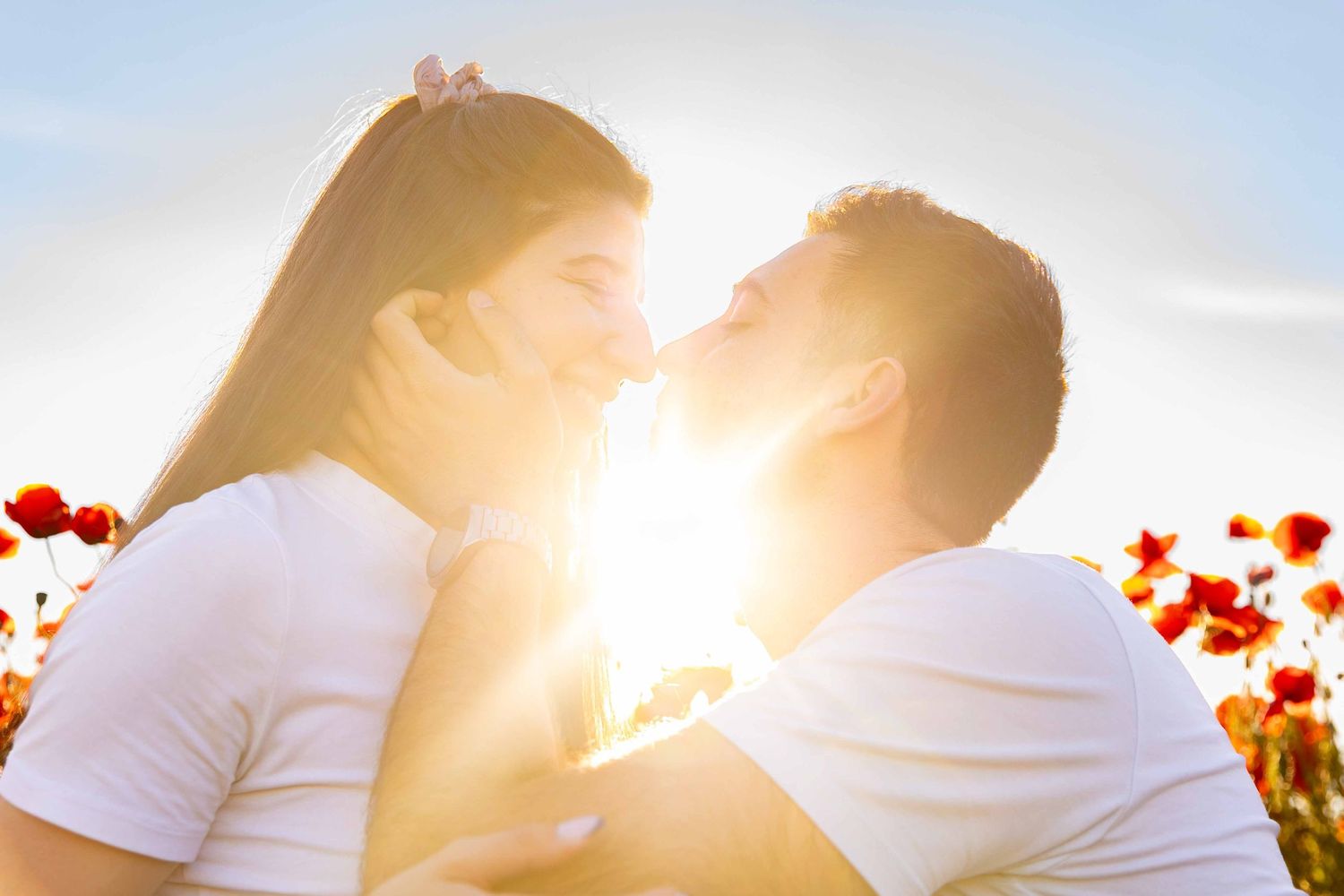 Romantic silhouette couple embracing against dramatic sunset sky with orange backlight and lens flare effect.