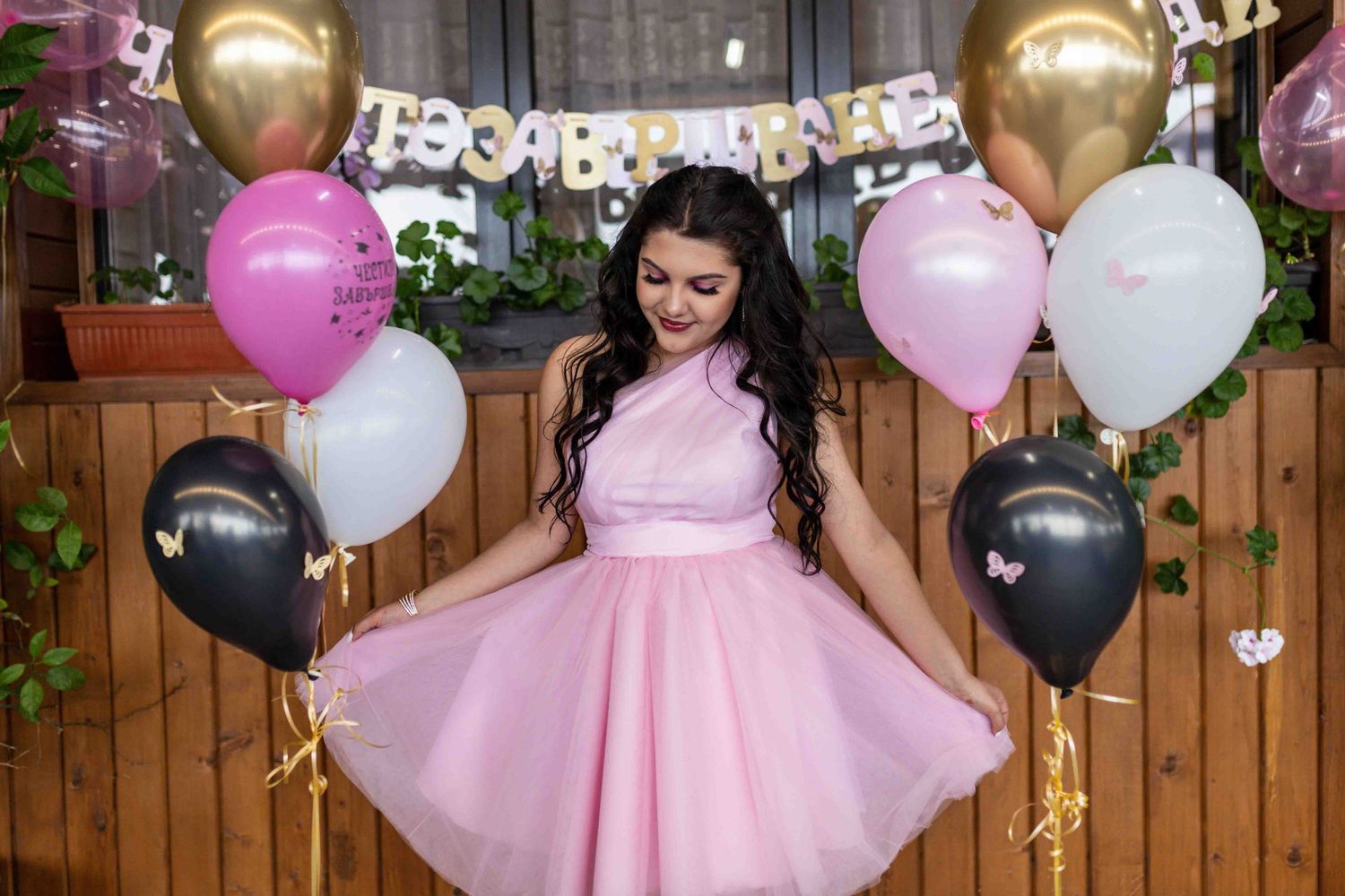 A celebratory scene with pink and black balloons surrounding a figure in a flowing pink formal dress.