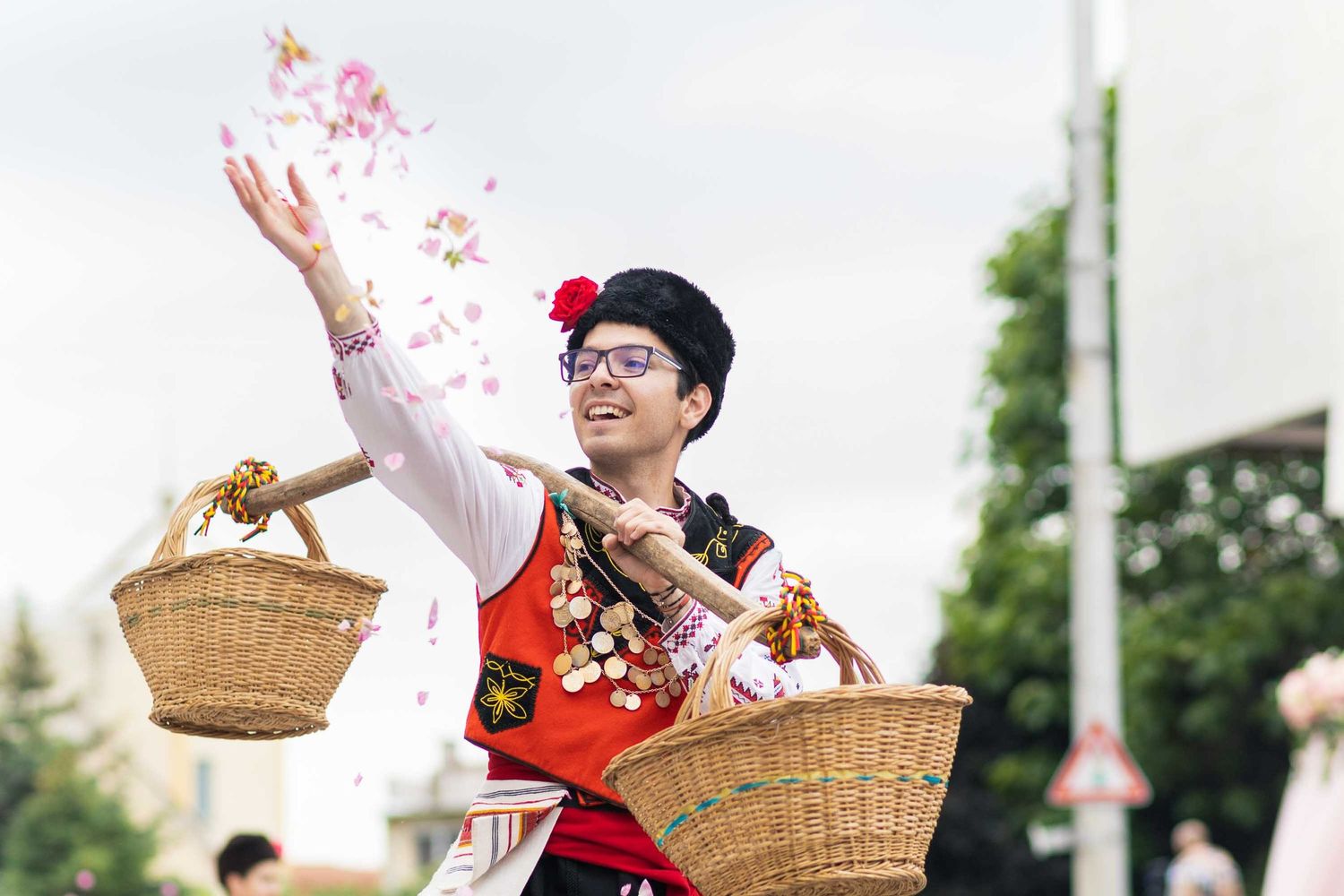 A performer releases red and white confetti from a woven basket during an outdoor celebration event.