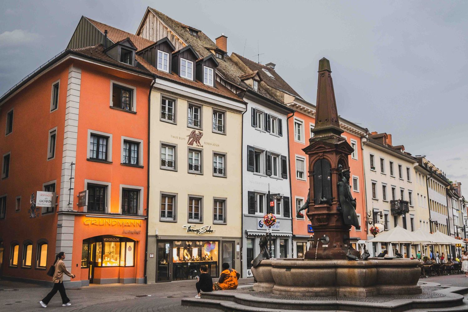 Historic German town facade with traditional architecture, old fountain, and rustic buildings along a cobblestone street.