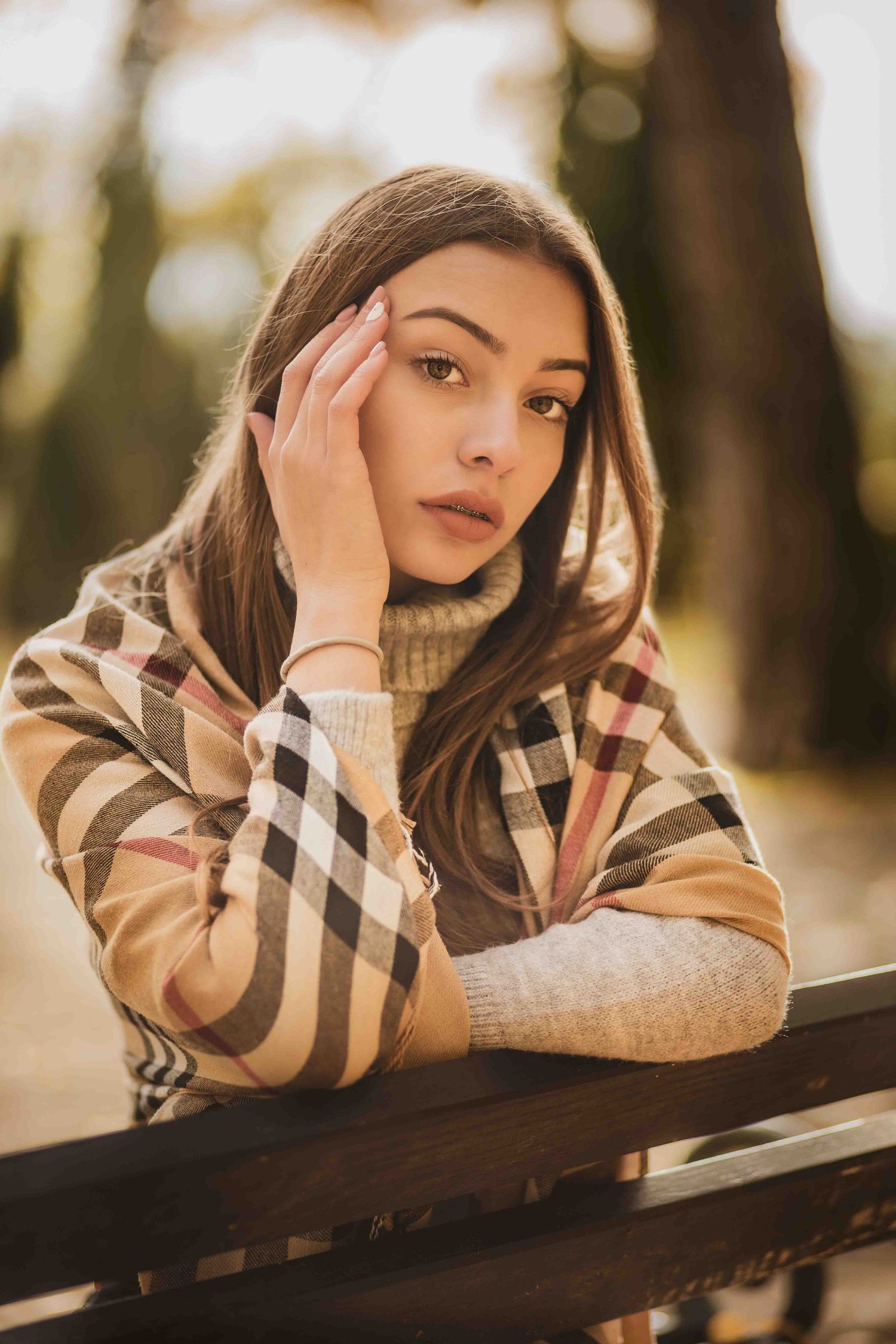 A contemplative figure in a plaid turtleneck sweater leans on a wooden railing during golden hour outdoors.