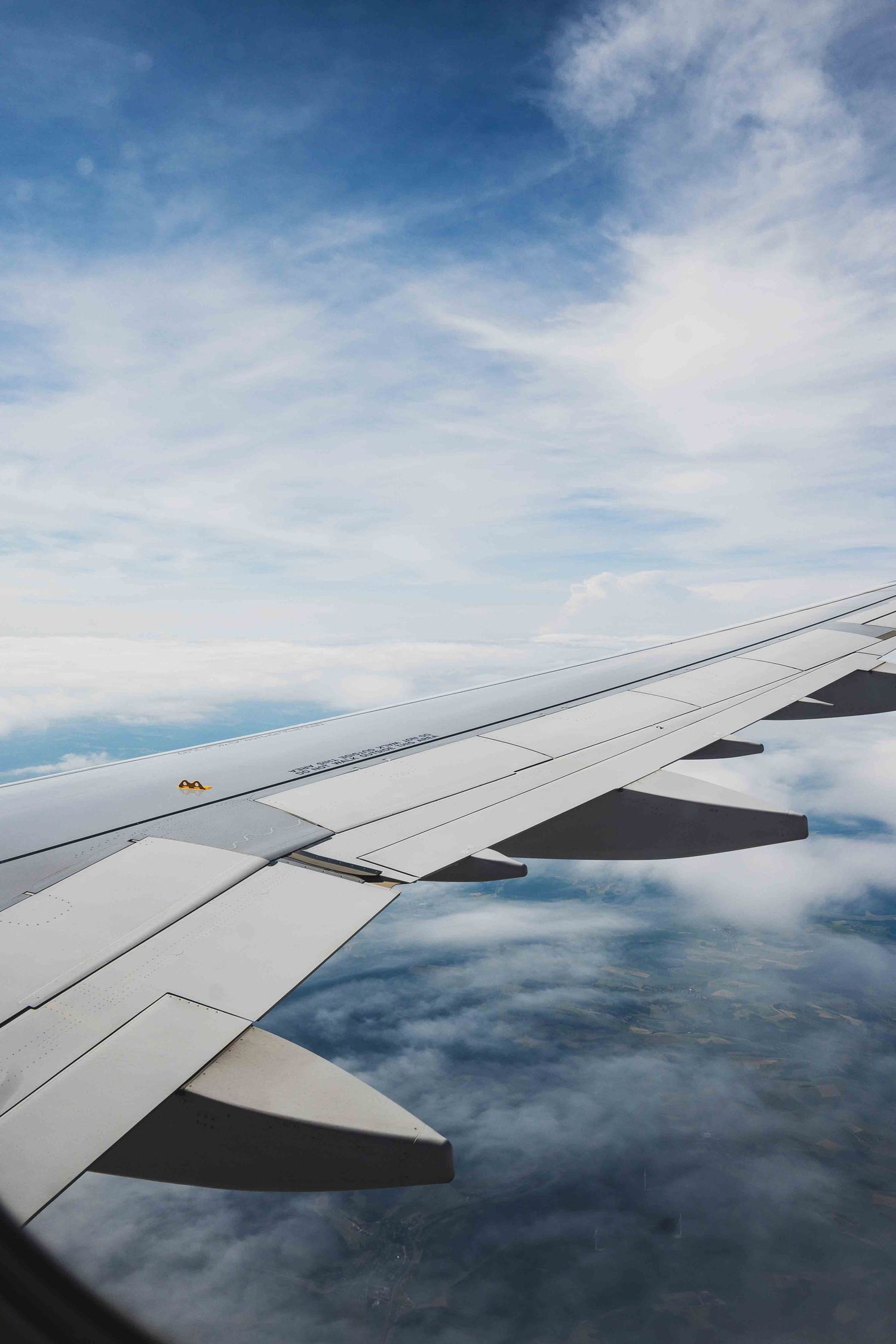 View of airplane wing against blue sky and white clouds during flight.