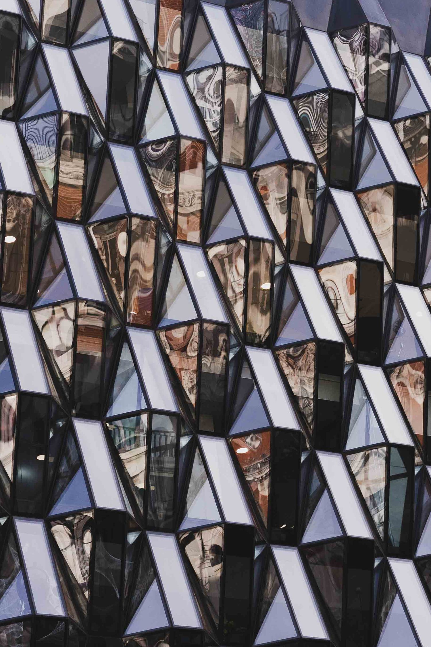 Abstract geometric pattern made of reflective glass panels showing fragmented architectural reflections in triangular shapes.