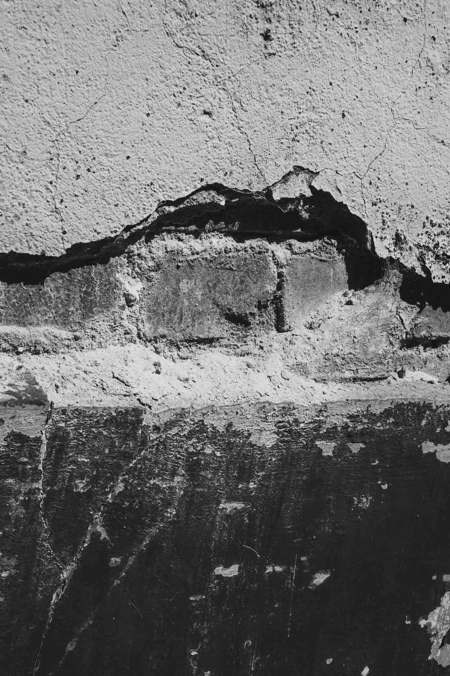 Black and white texture of damaged concrete wall showing exposed layers and deterioration.