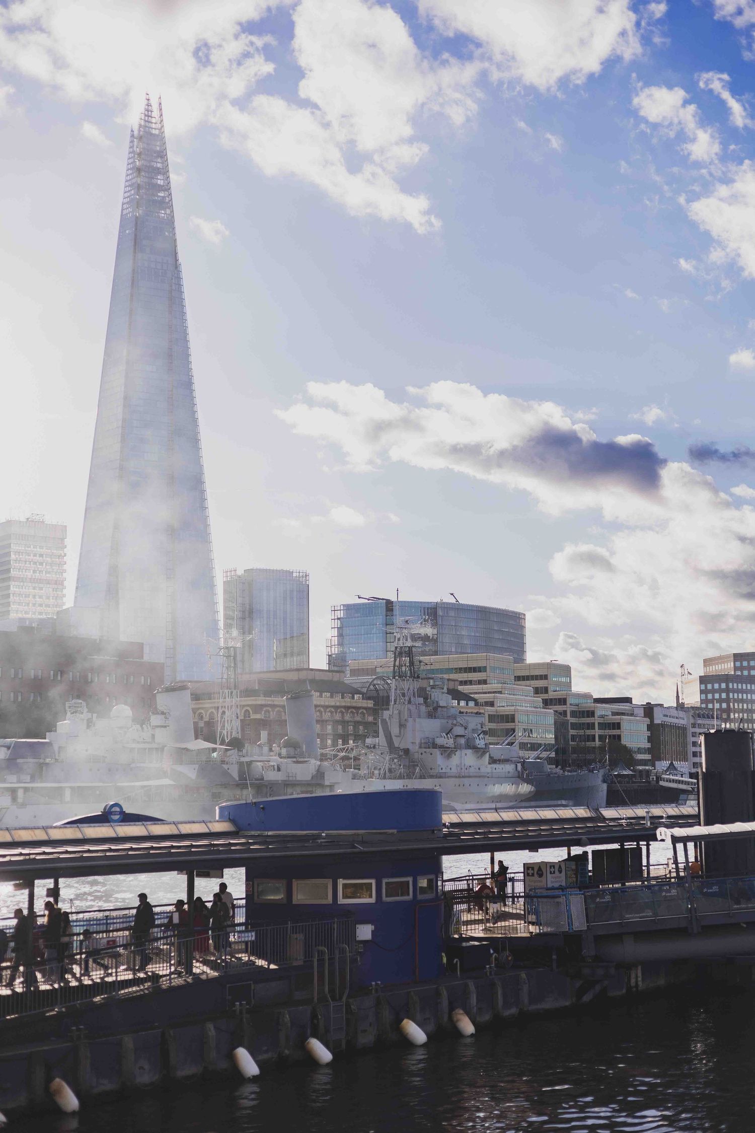 London skyline featuring The Shard skyscraper with dramatic cloudy sky and waterfront buildings along the Thames River.