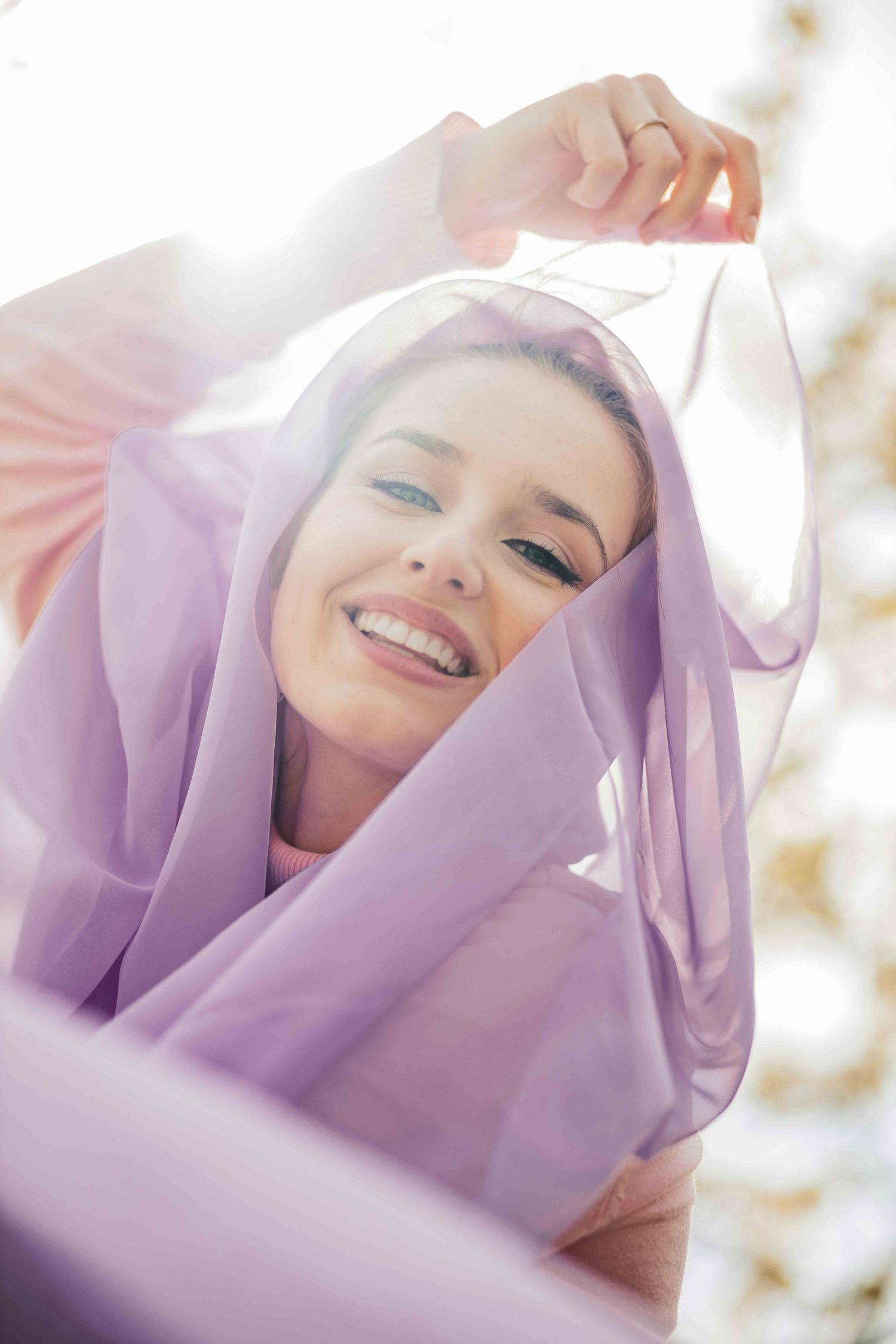Joyful portrait draped in flowing lavender fabric with soft sunlit glow.