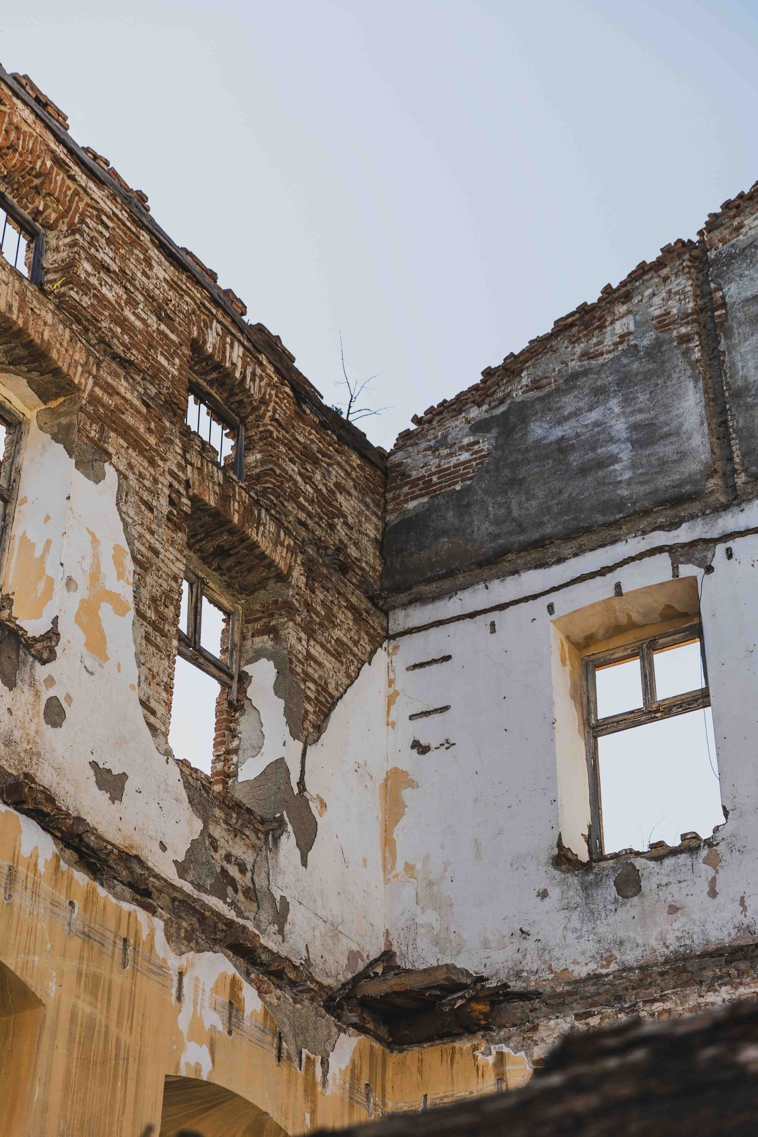 Crumbling stone walls and broken windows of an abandoned building with exposed structural damage.