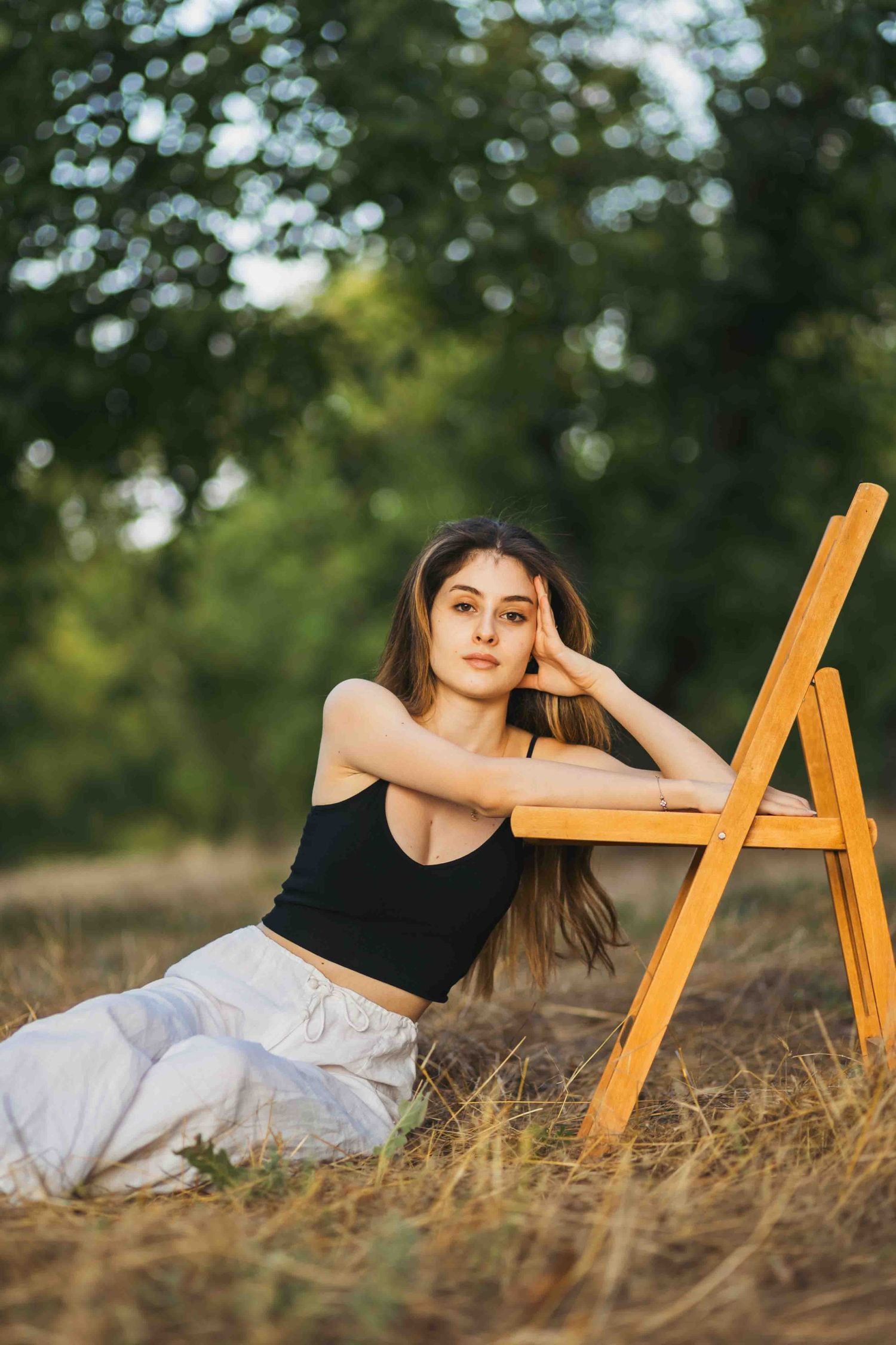 A figure reclines in a grassy field next to a wooden ladder at golden hour, creating a dreamy outdoor portrait scene.