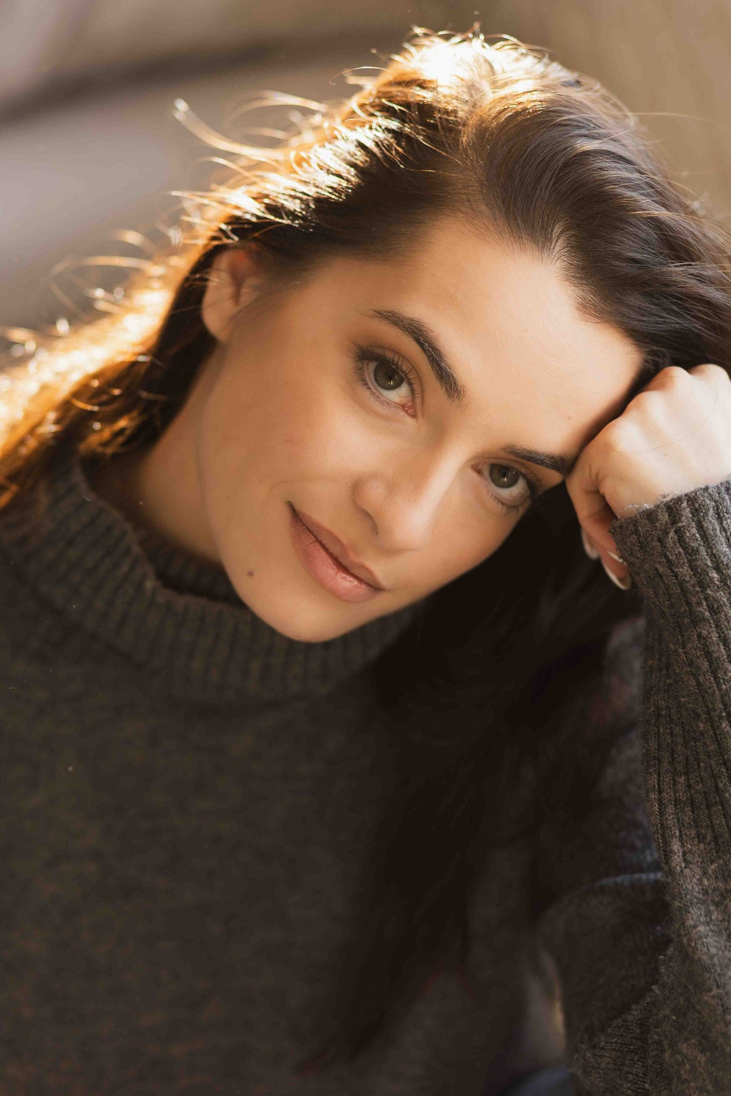 Soft indoor portrait of someone wearing a dark turtleneck sweater with glowing rim light in their hair.