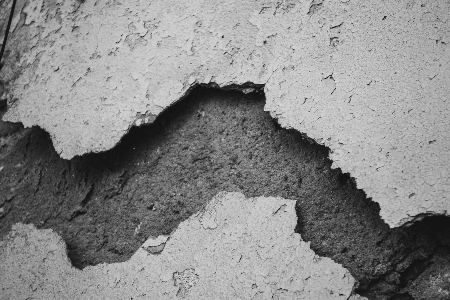 Close-up black and white photo of damaged wall showing crumbling plaster and exposed inner surface texture.
