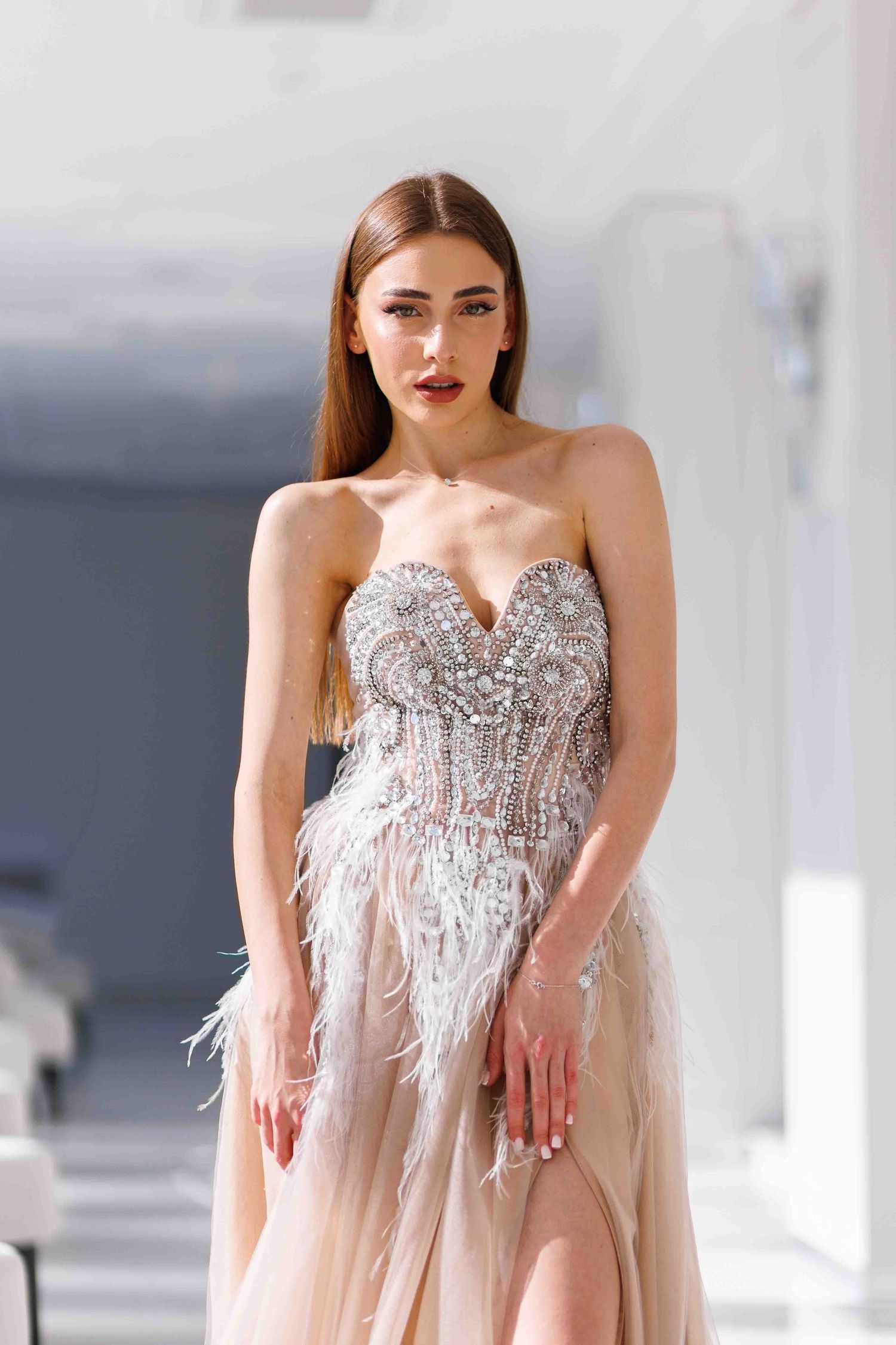 Elegant blush gown with sweetheart neckline features intricate beading and delicate feather details on a sheer silhouette.
