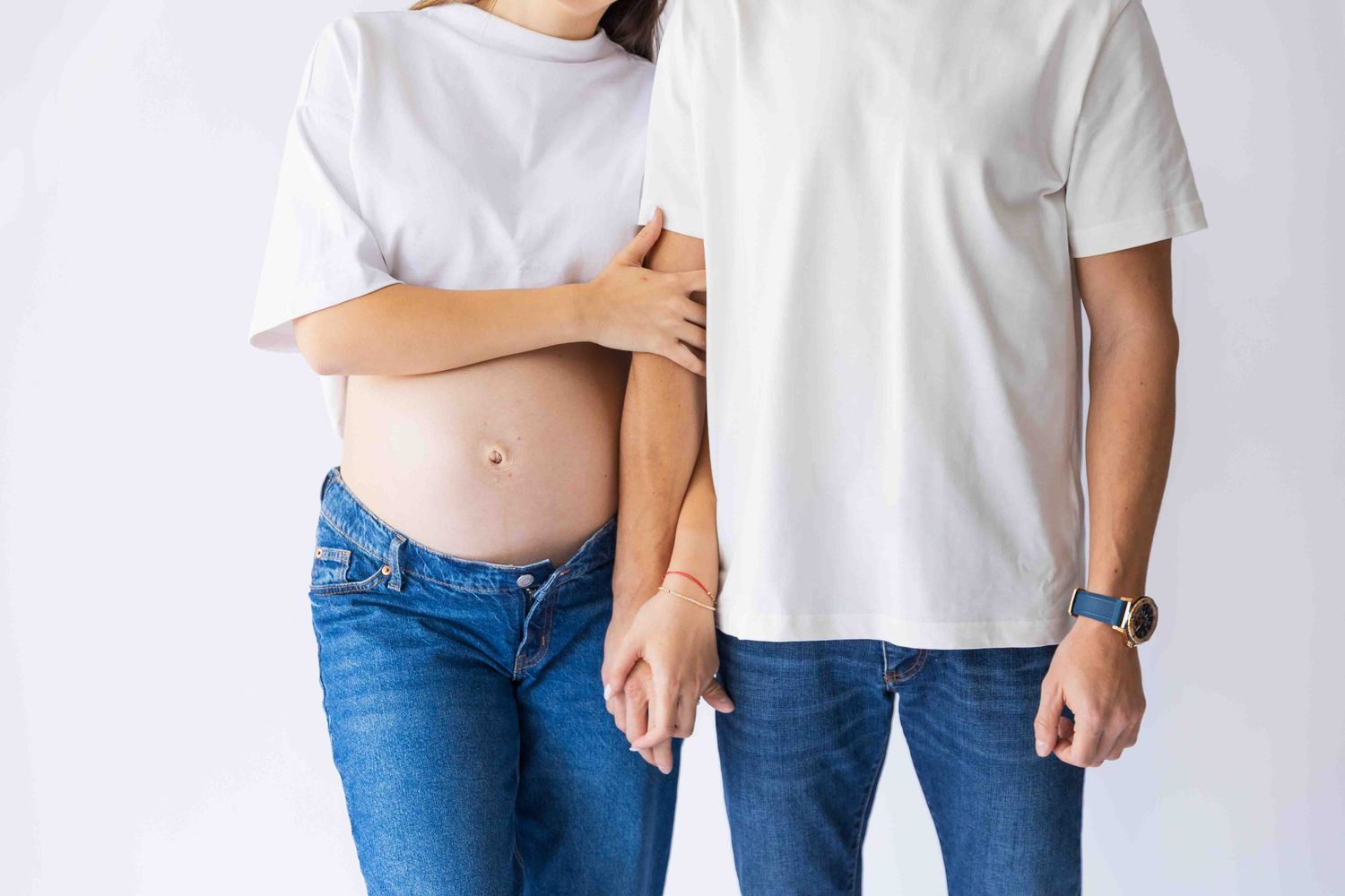 Cropped view of someone wearing blue jeans and a white t-shirt posing with hands in pockets against white background.