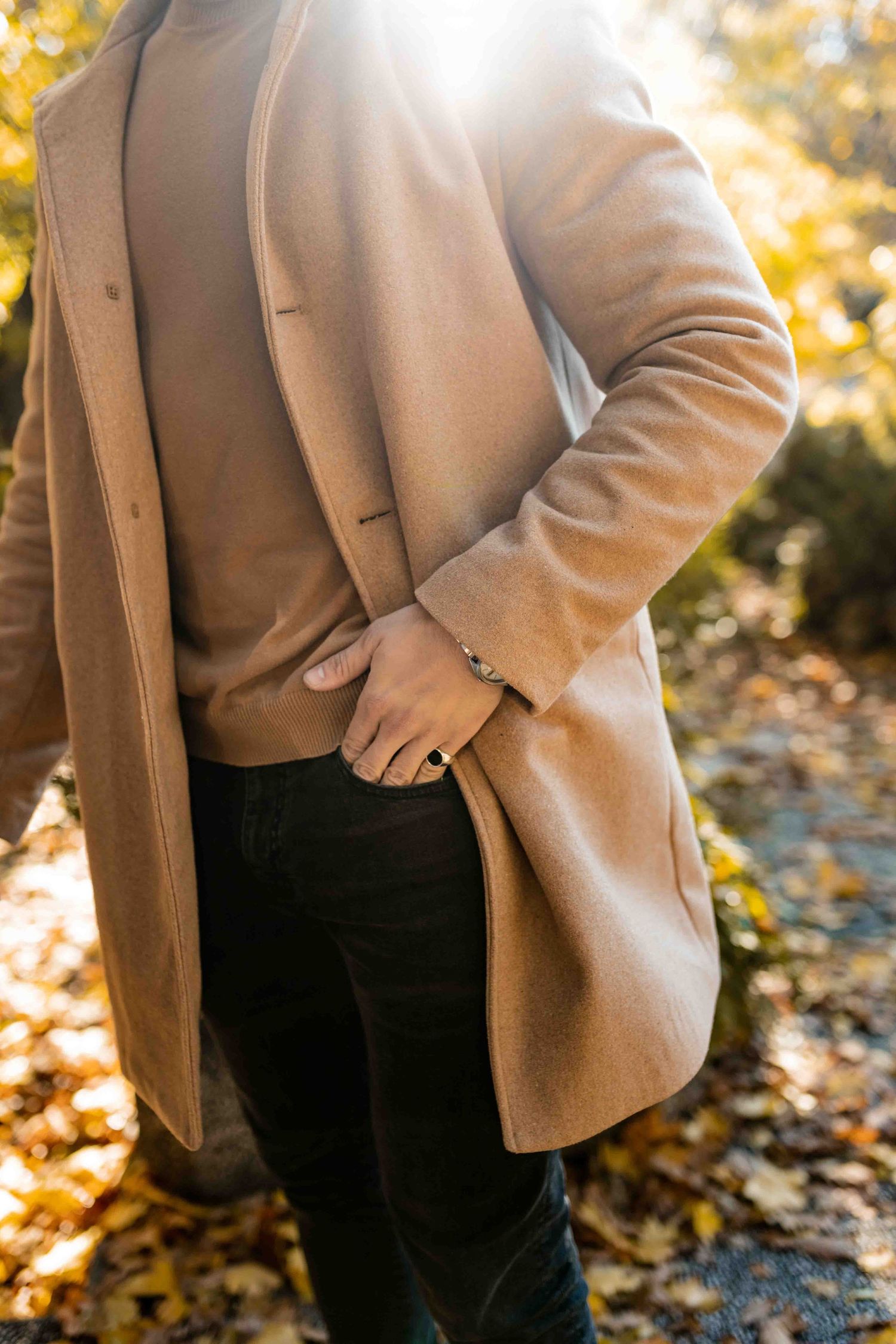 Close-up view of someone wearing a beige blazer and dark pants against an autumn background with golden leaves.