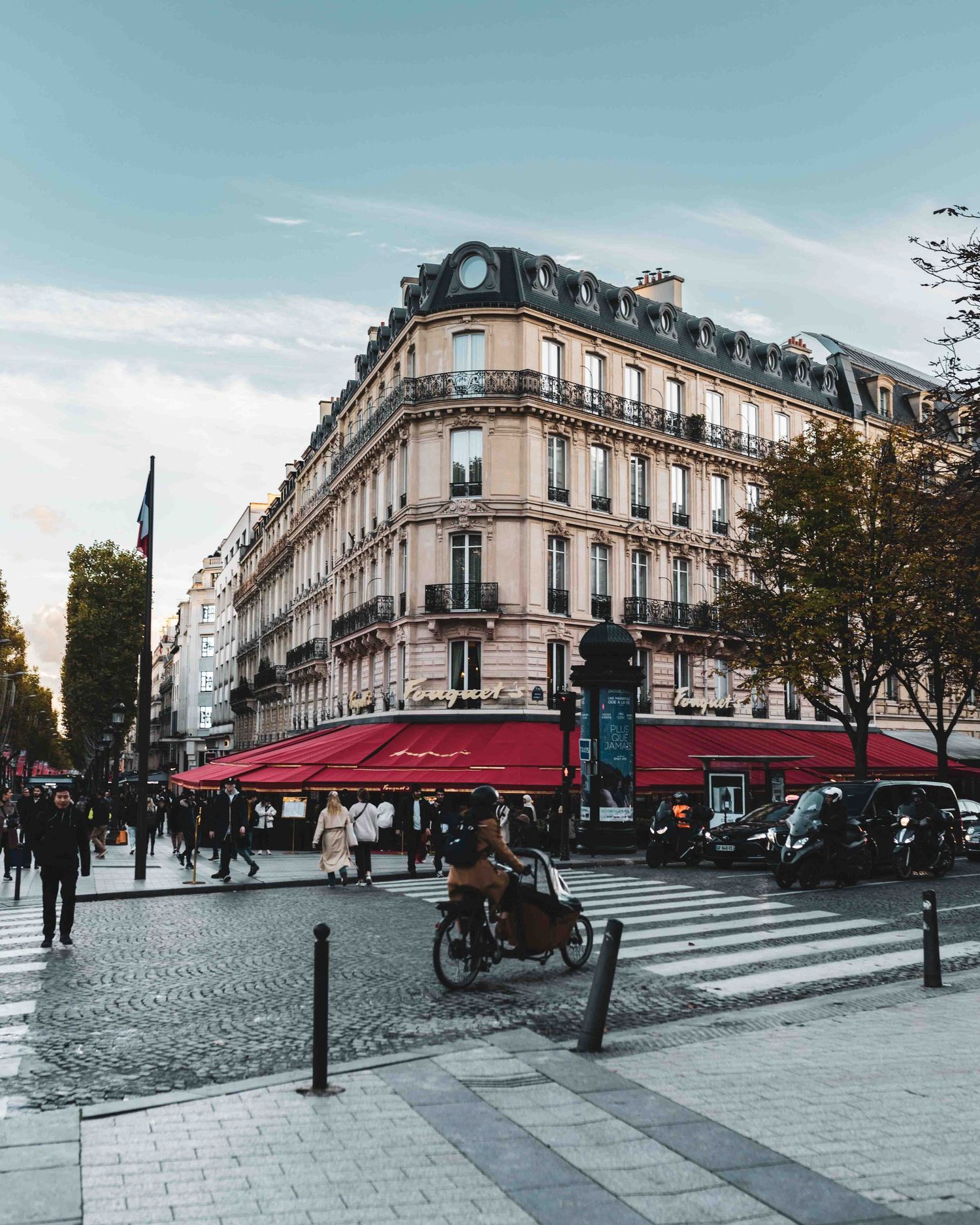 Classic Parisian street corner with Haussmann architecture building and red awning cafe on a cloudy day.