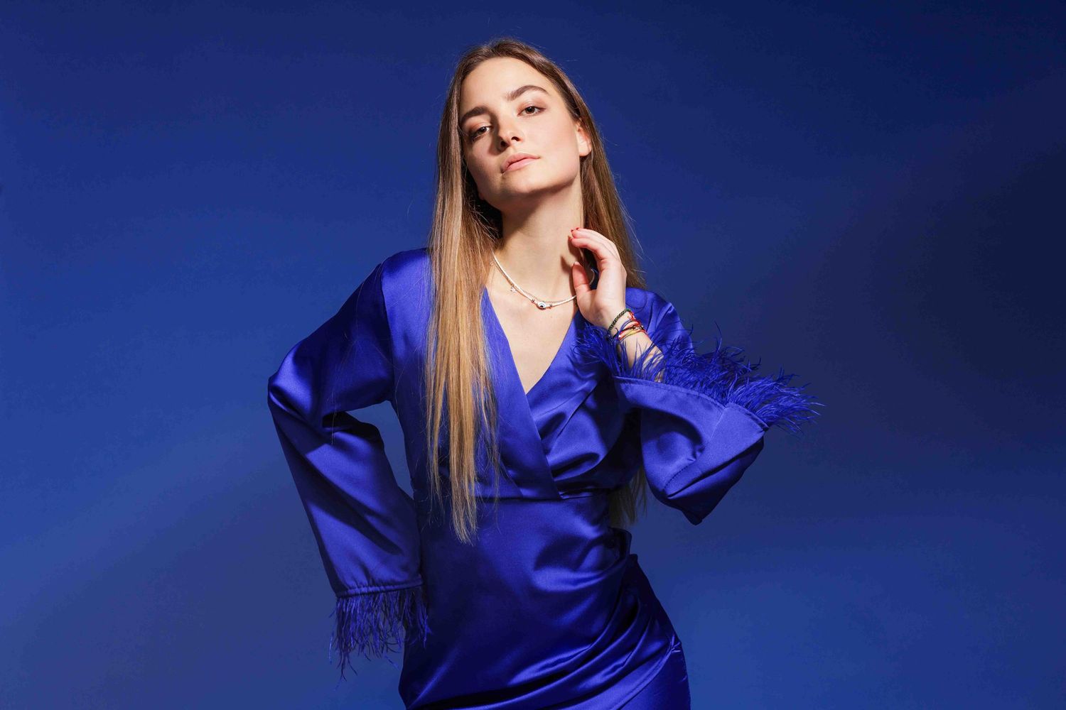 A woman poses confidently in a royal blue silk dress against a dark blue studio background.