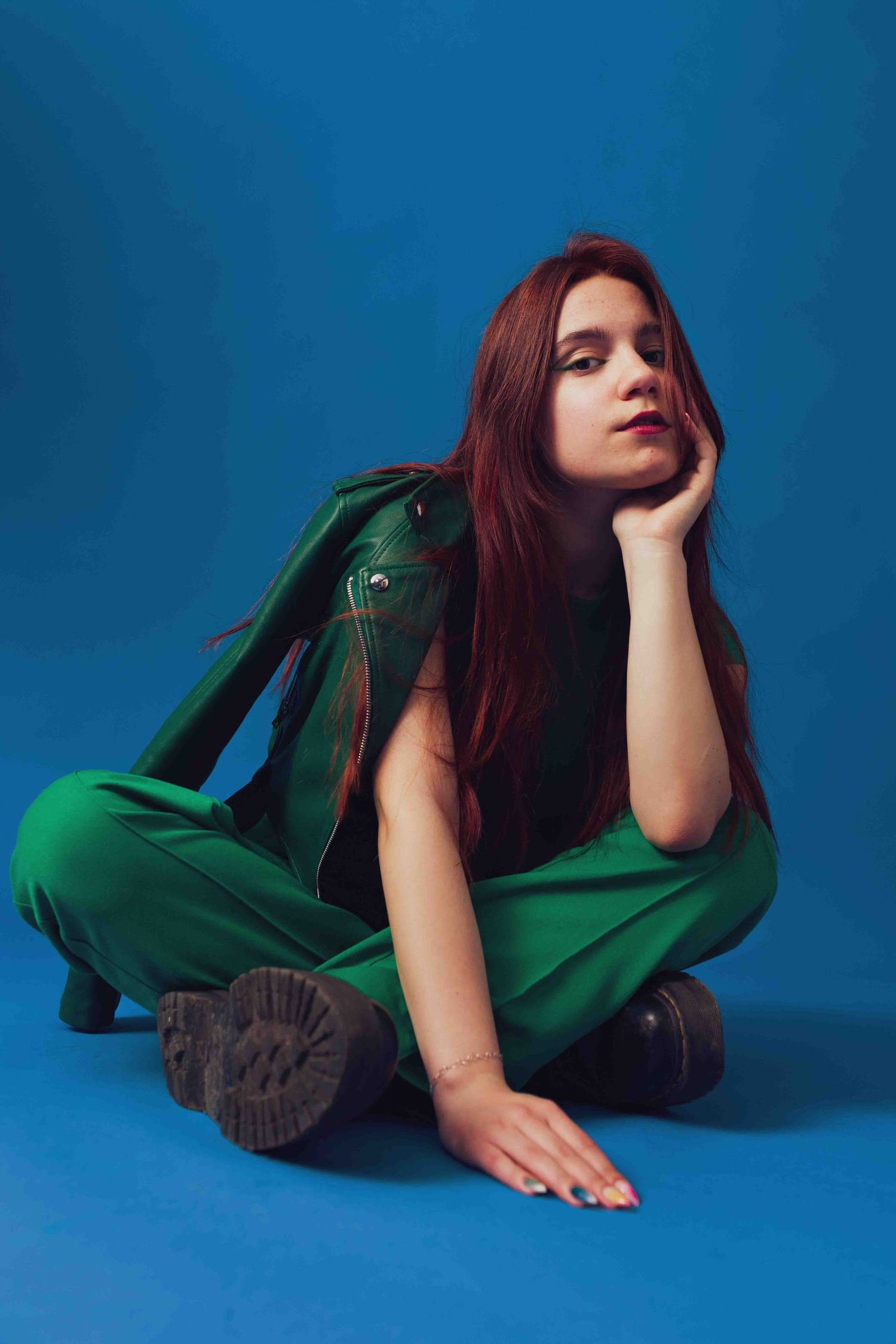 Fashion model in emerald green blouse poses artistically against blue backdrop in a series of dynamic shots.