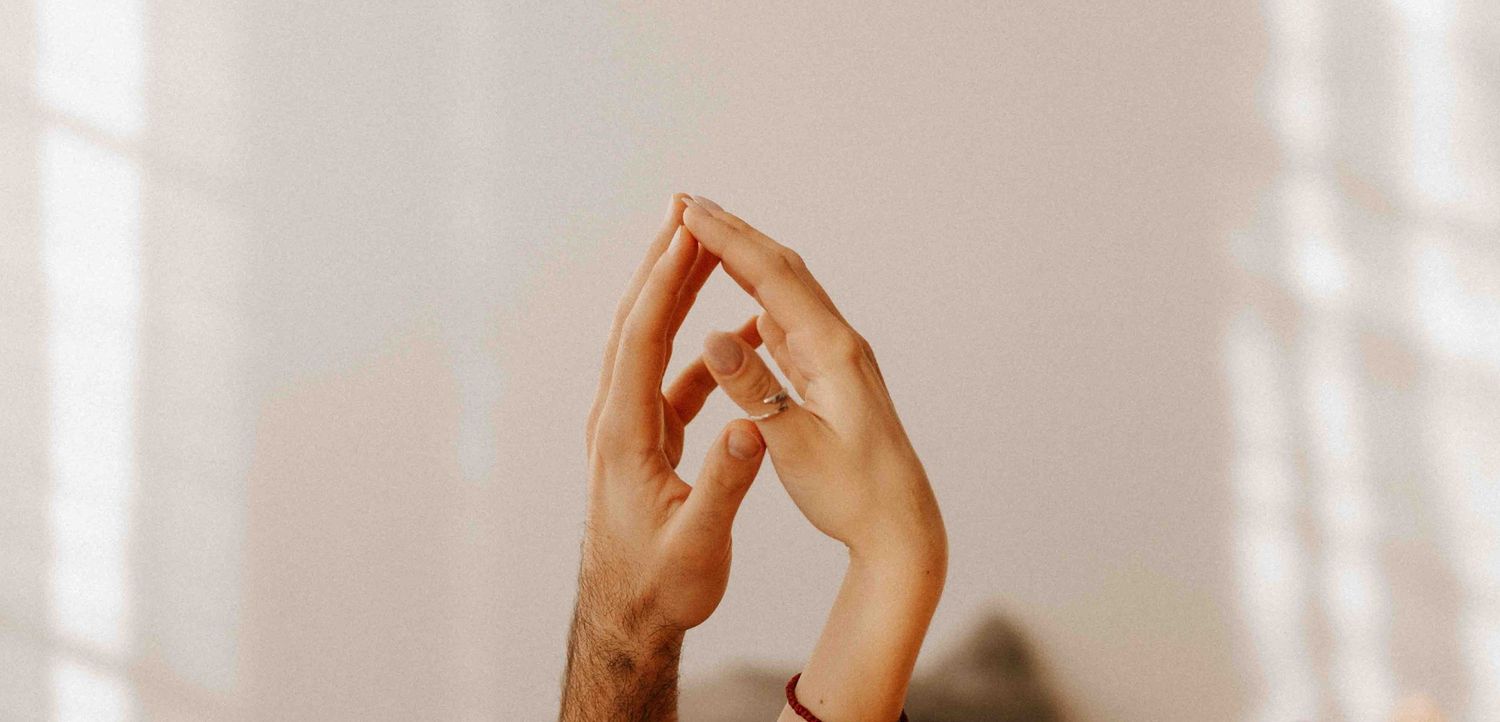 Two hands elegantly reaching towards each other in soft warm lighting against a light neutral background.