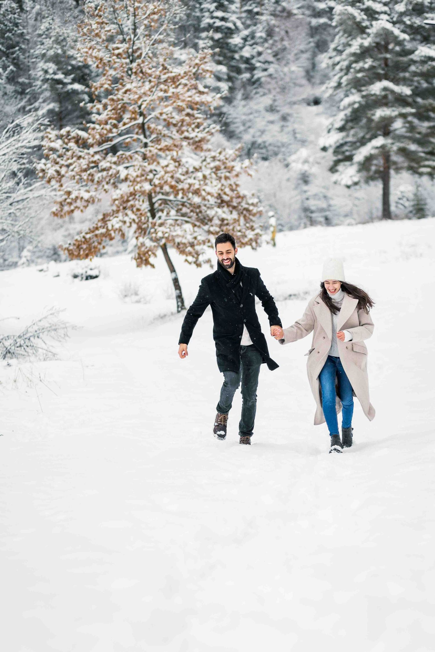 Two people running together through a snowy winter landscape with snow-covered trees in the background.