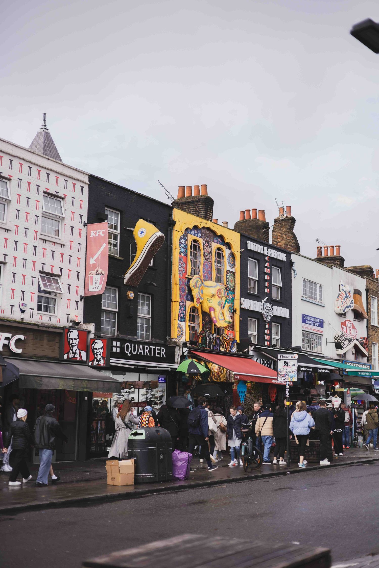 Busy Camden High Street in London with colorful shop fronts and pedestrians walking past KFC and other retail stores.