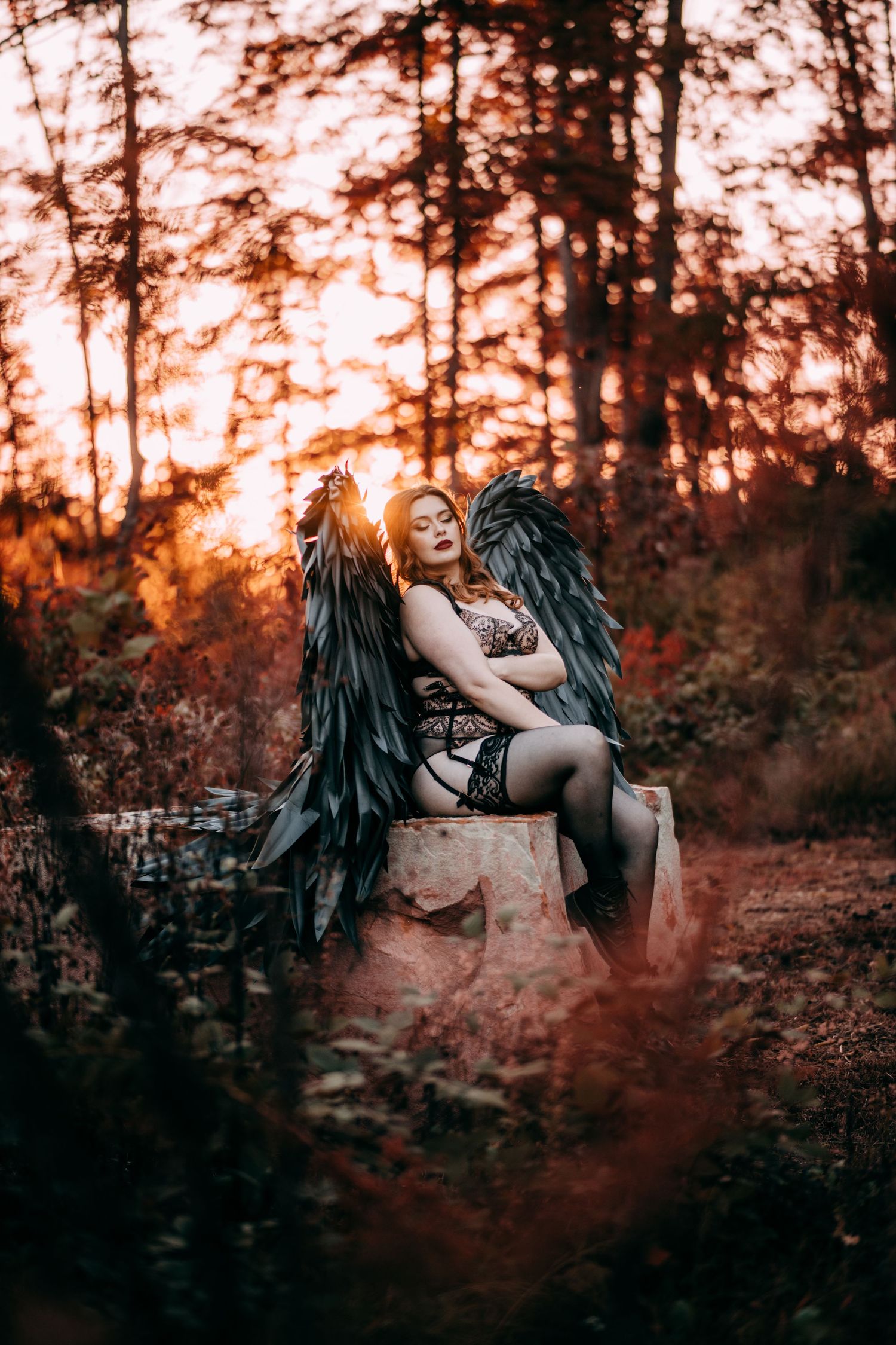 Fantasy portrait of a figure with dark angel wings sitting on a rock at sunset in a moody forest setting. Vanceburg Ky