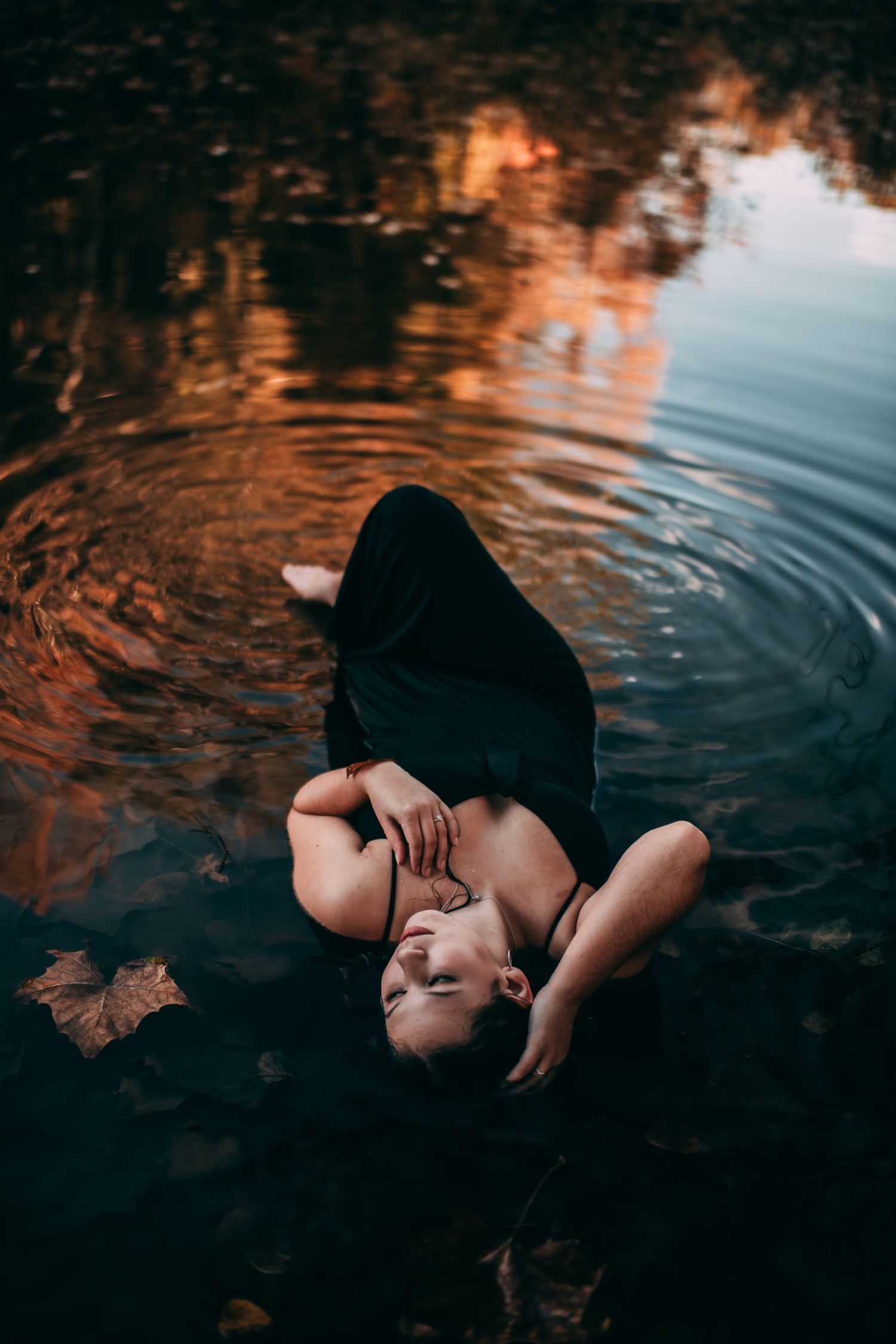 Artistic water portrait with dark dress creating ripples at sunset.