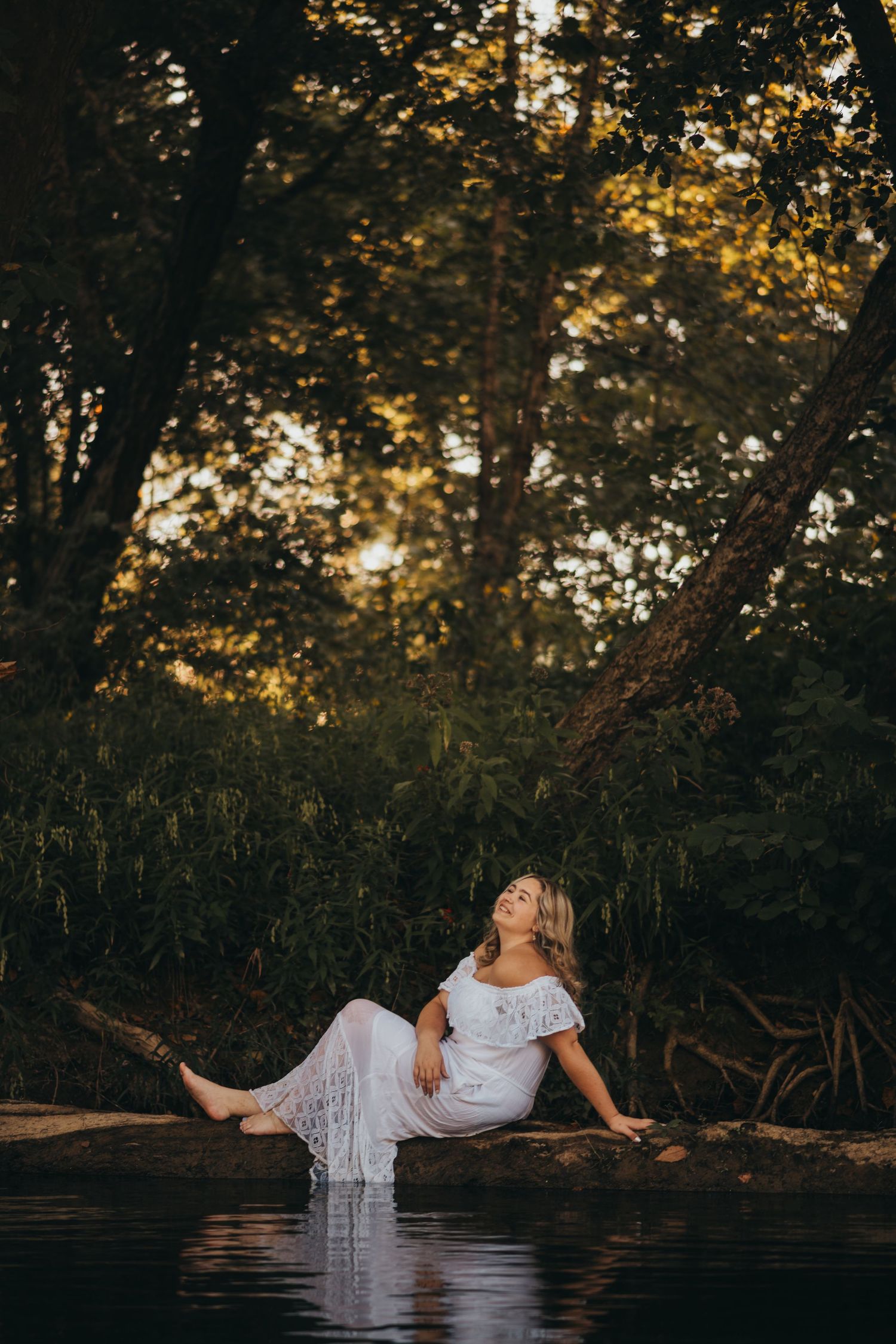 A white dress flows gracefully in a serene water setting during a dreamy outdoor photoshoot at sunset.