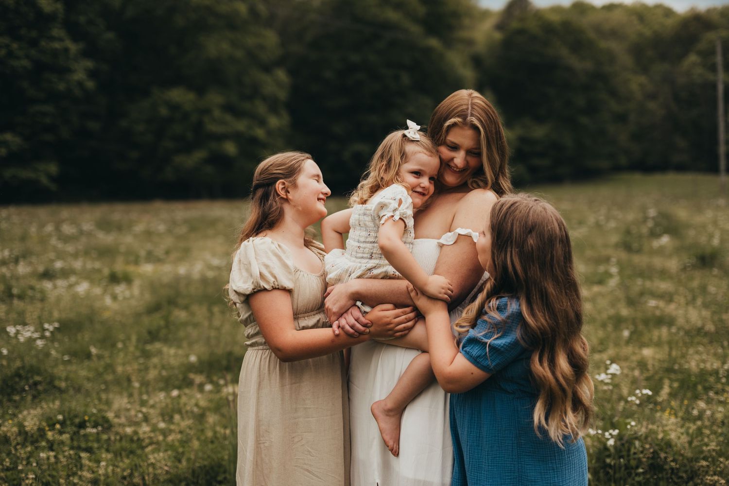 A group of people wearing blue and cream colored dresses embrace in a sunny meadow during a photo session.
