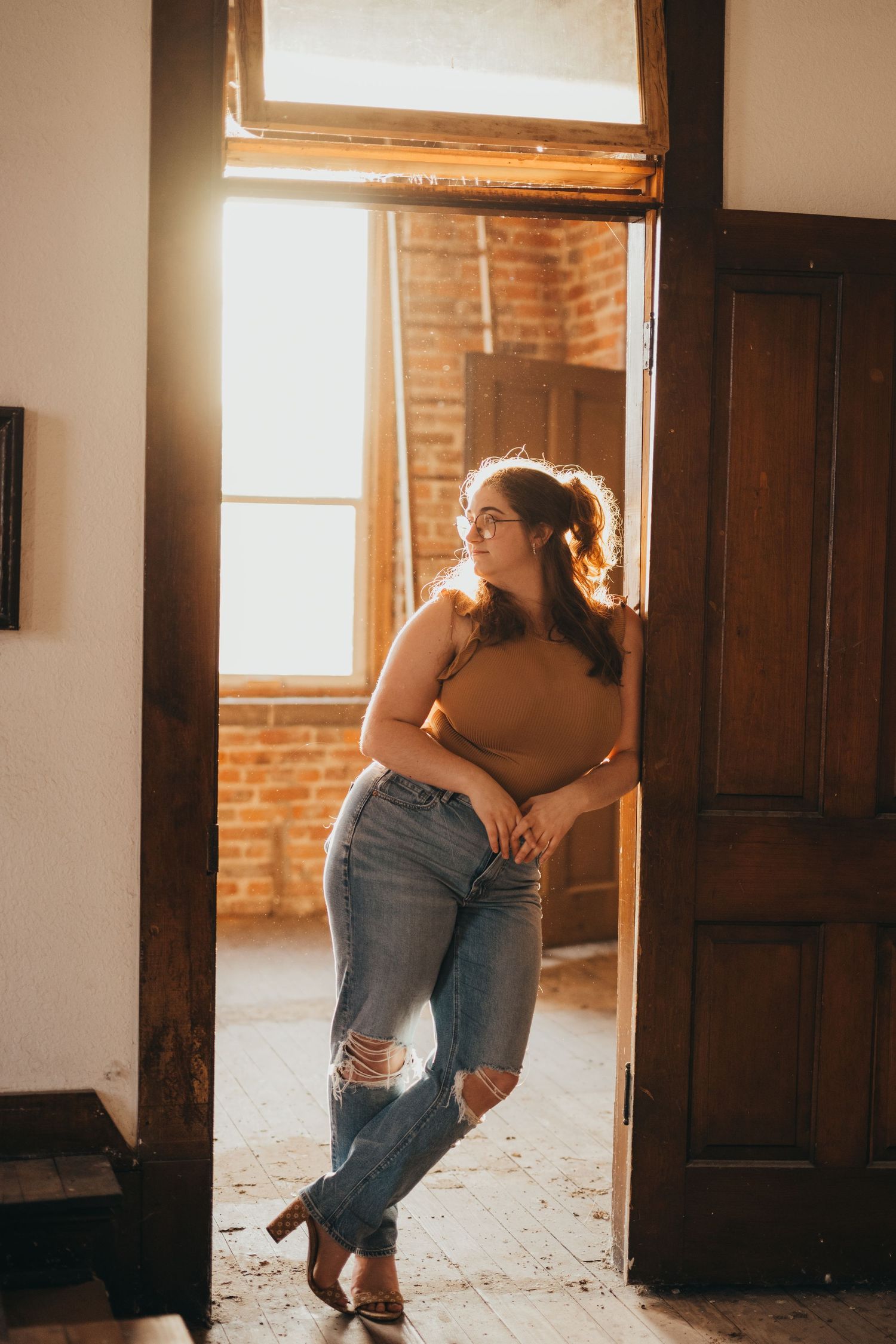 A couple embraces in a rustic room with exposed brick walls and wooden doors as warm sunlight streams through windows.