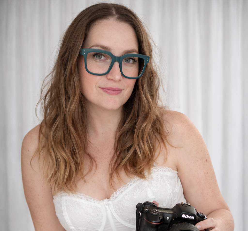 A person wearing stylish blue glasses and a white lace top poses with a vintage camera.