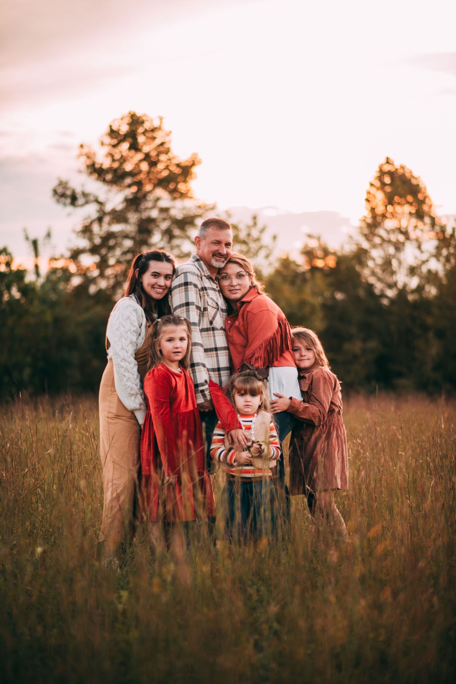 A family stands together in a golden field at sunset with trees silhouetted in the background. Vanceburg Ky