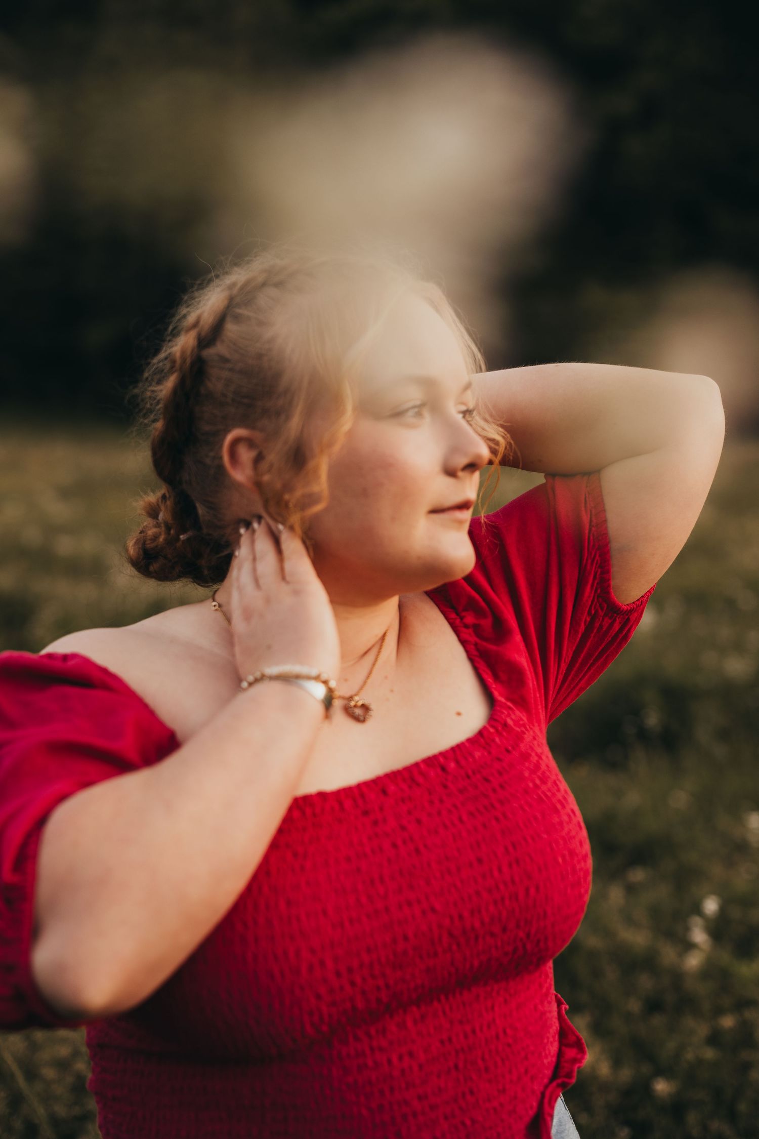 Person in red dress poses artistically against natural outdoor setting.