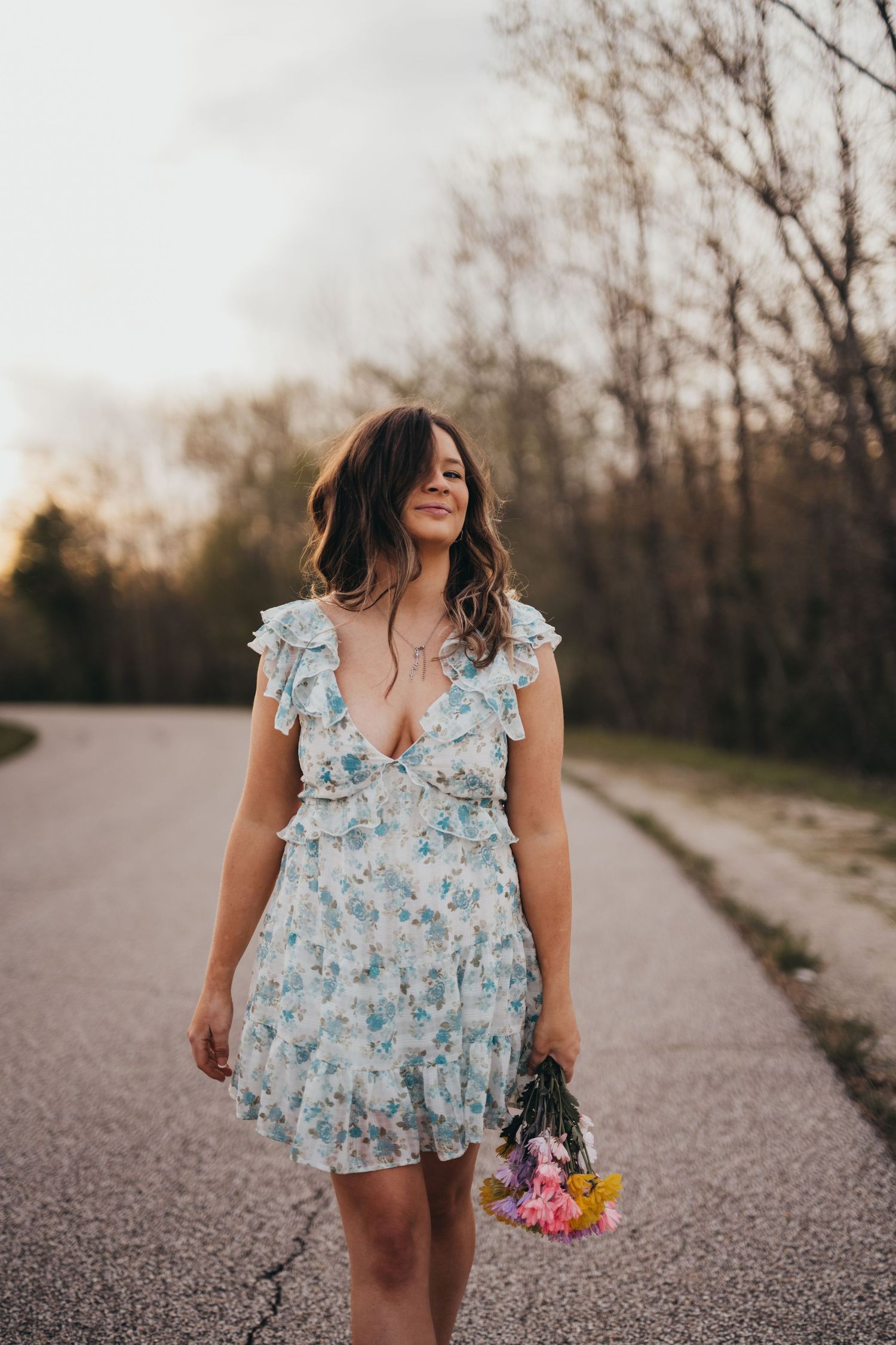 Person in floral dress walking down gravel path holding colorful flowers.