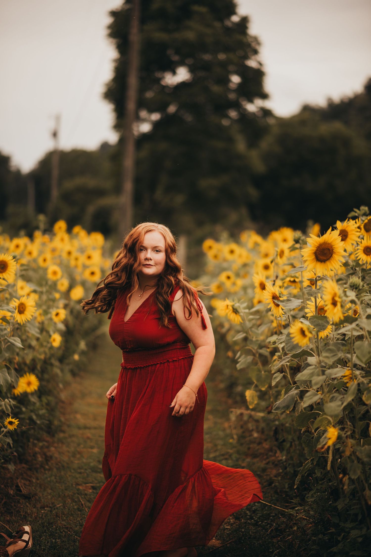 A flowing red dress twirls gracefully among vibrant yellow sunflowers in a summer field.
