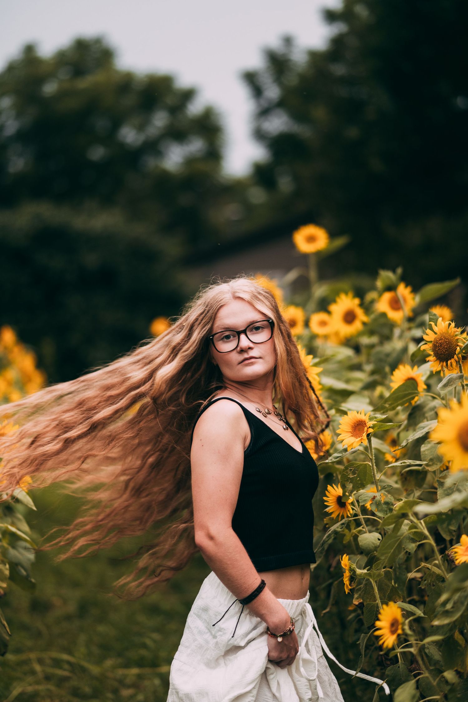 Long-haired figure twirls joyfully in sunflower field wearing black and white outfit.