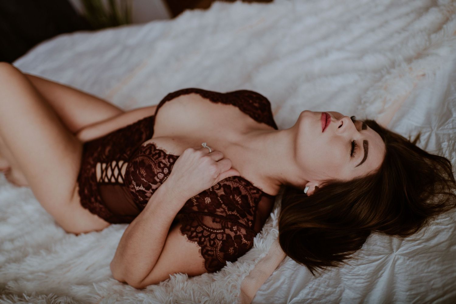 Person wearing lace lingerie poses seductively on white bedding in romantic boudoir photoshoot. Vanceburg Ky