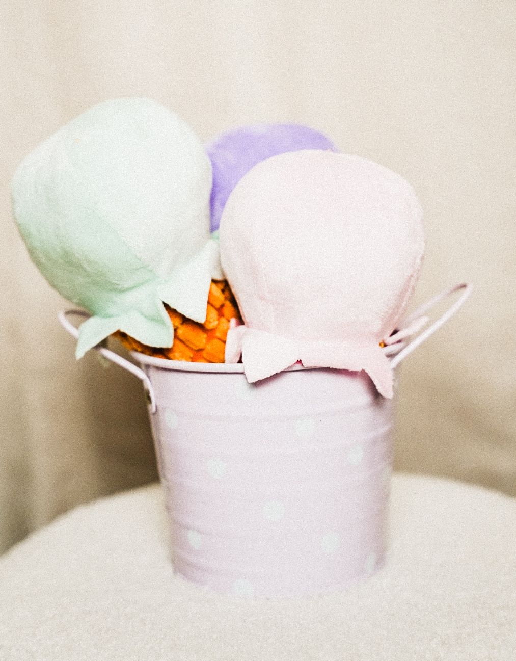 Three pastel fabric balloons in mint, lavender, and pink displayed in a polka dot pale pink metal bucket.