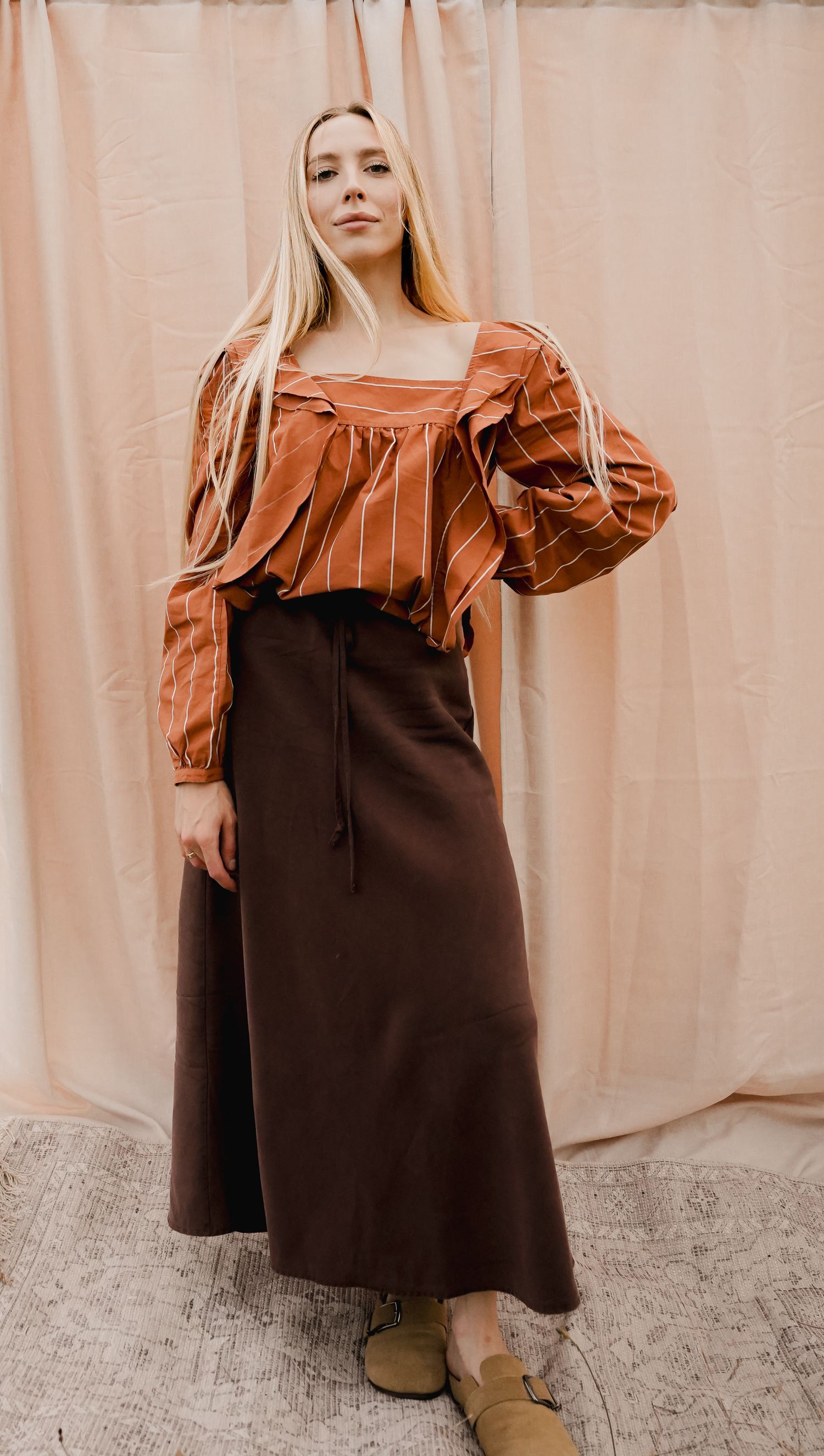 Woman wearing rust striped square-neck blouse with puff sleeves and dark brown maxi skirt with tie waist.