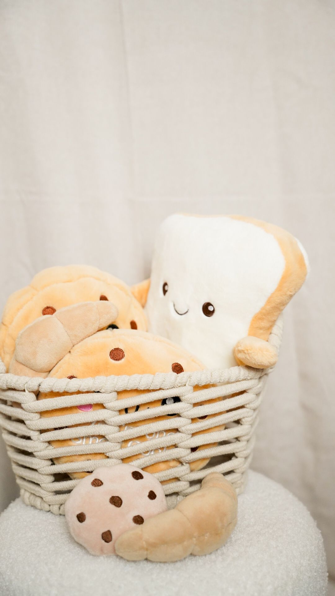 A wicker basket filled with cute kawaii plush toys shaped like bread toast and chocolate chip cookies on a white background.