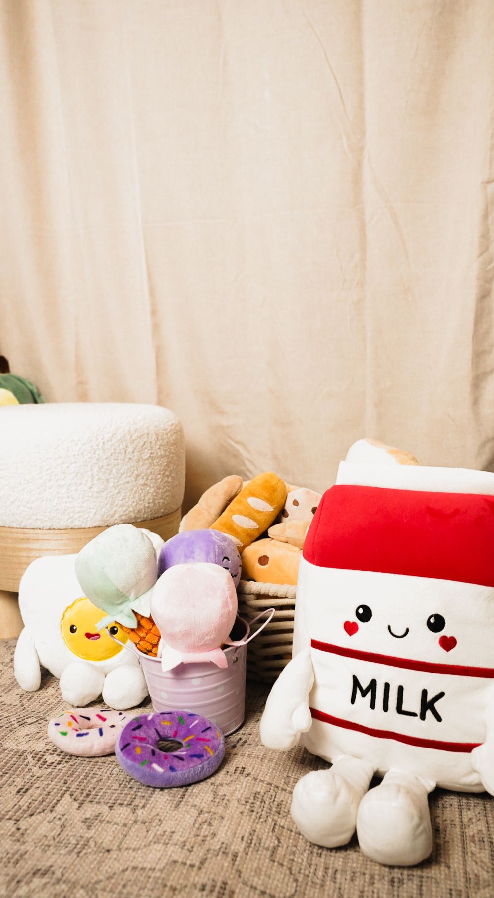 Cute kawaii food plush toys including a milk carton, donut, and bread loaves arranged on a rug with a basket.