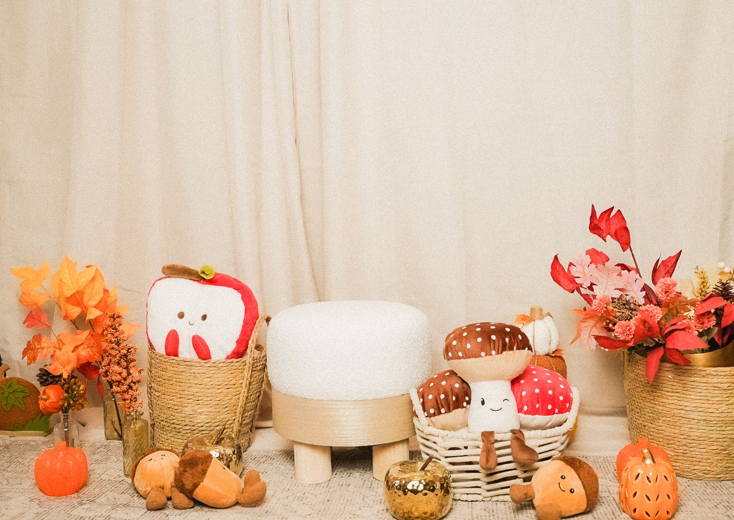 Fall harvest display with apple and mushroom plush toys, pumpkins, and autumn floral arrangements in wicker baskets.
