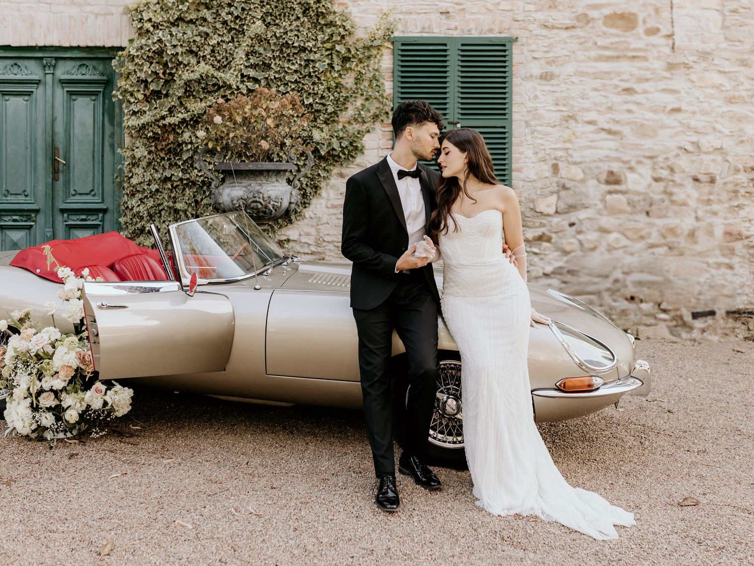Elegant wedding photo series showcasing classic car and romantic couple moments against stone wall backdrop.