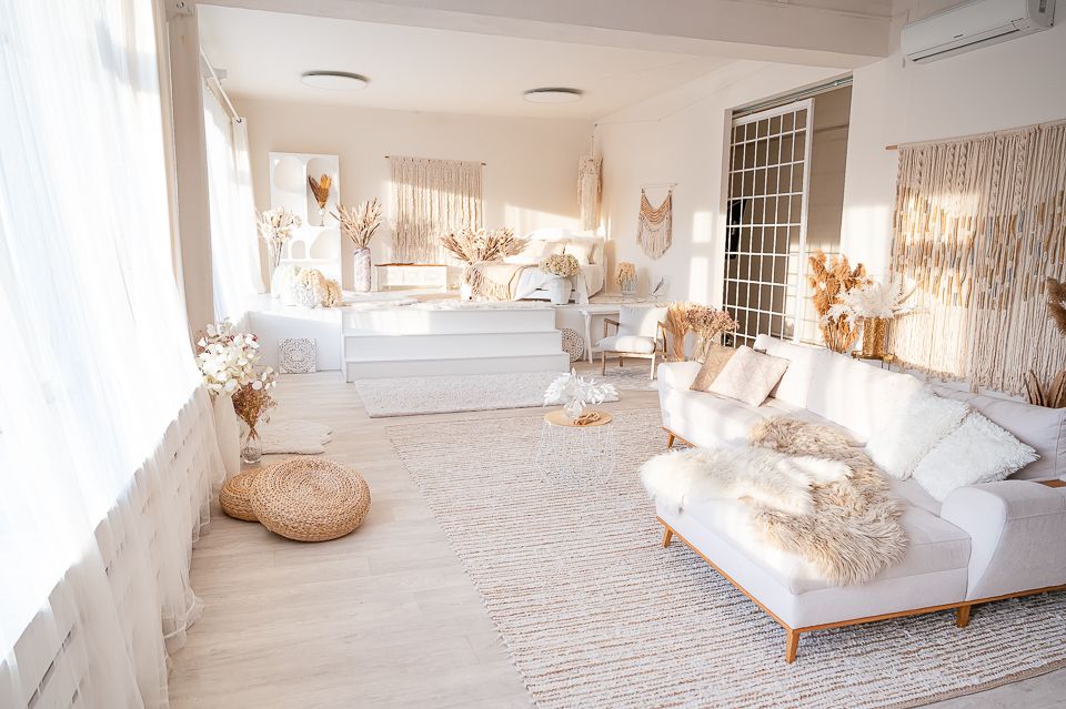 Bright boho living room with white sofa, fur pillows, woven rug, dried florals, and macrame wall decor in neutral tones.