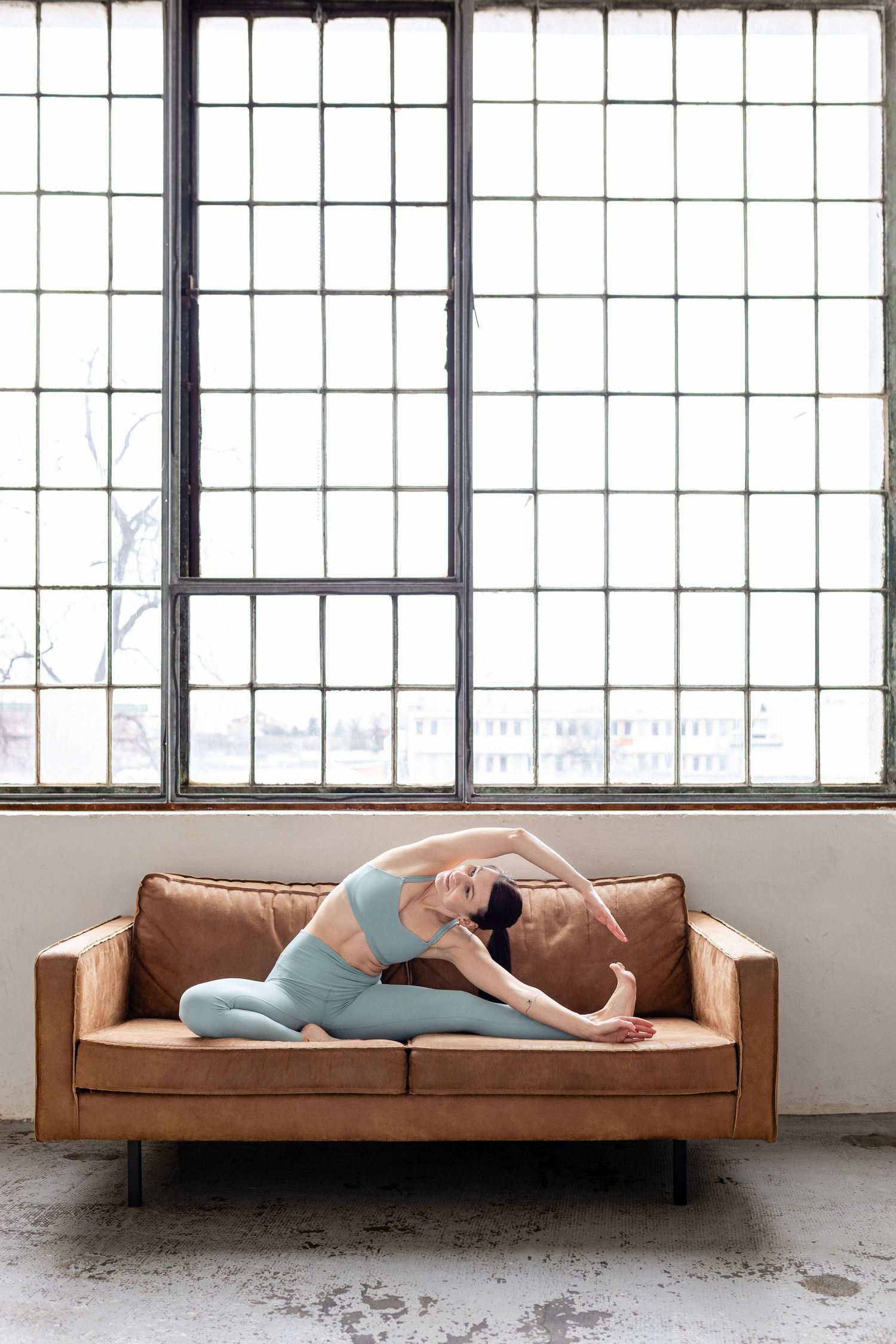A sequence of five photos showing someone lying on a brown leather couch in a bright industrial loft space.