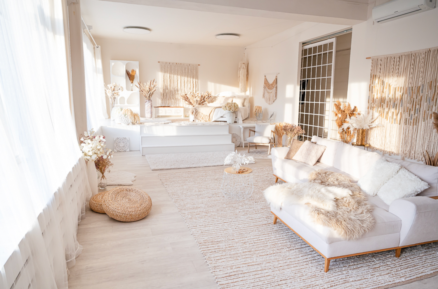 Bright boho living room with white sofa, fur throws, dried pampas grass, woven rug, and neutral decor in warm sunlight.