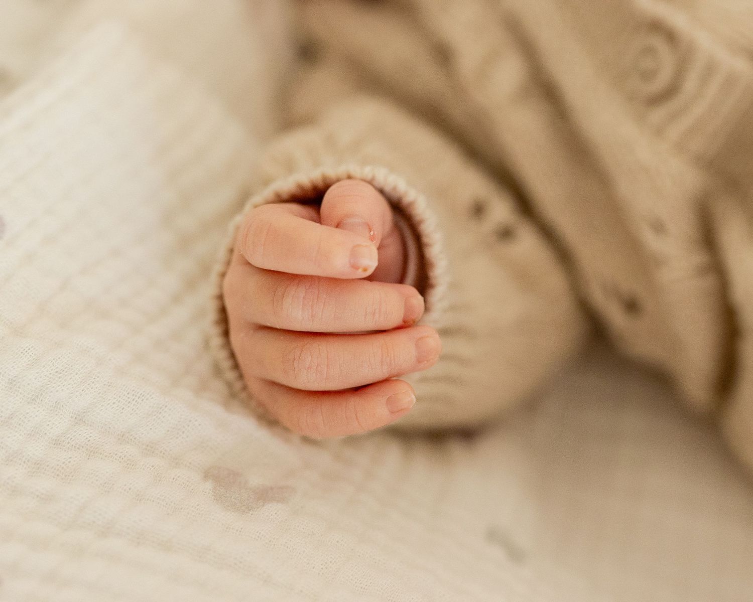 Close-up of a newborn baby's tiny clenched fist resting on a soft white textured blanket.