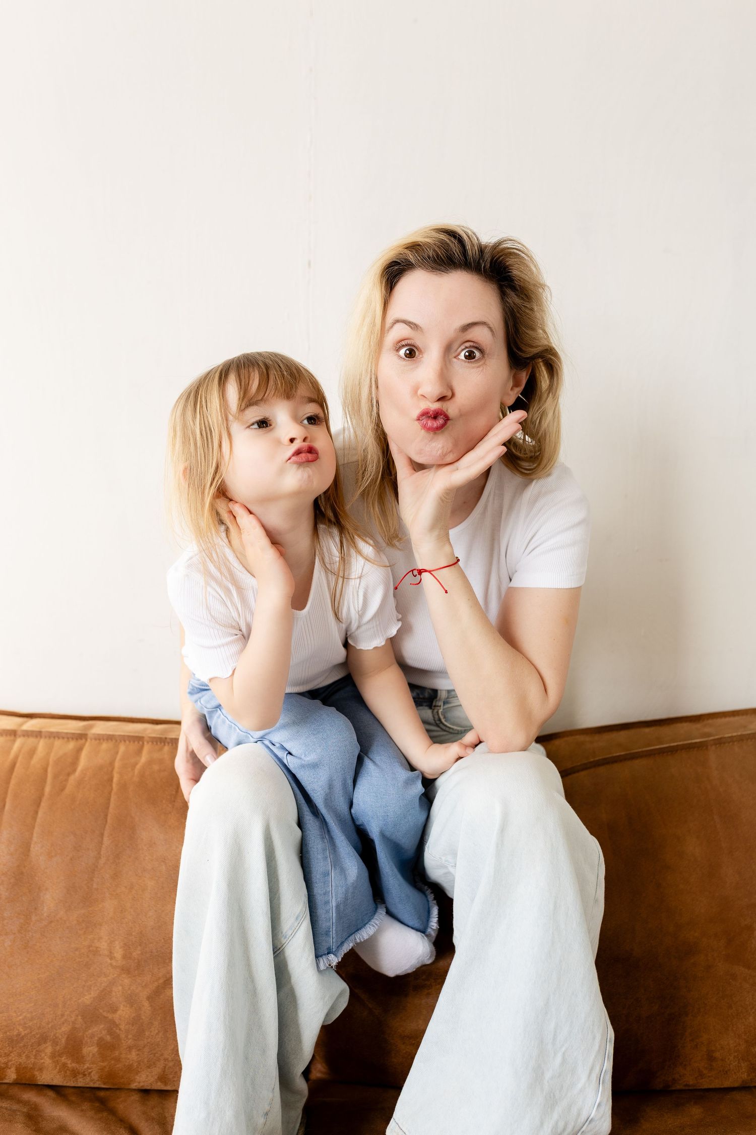 A parent and child in white outfits sit on a brown couch making playful faces in a three-photo collage.