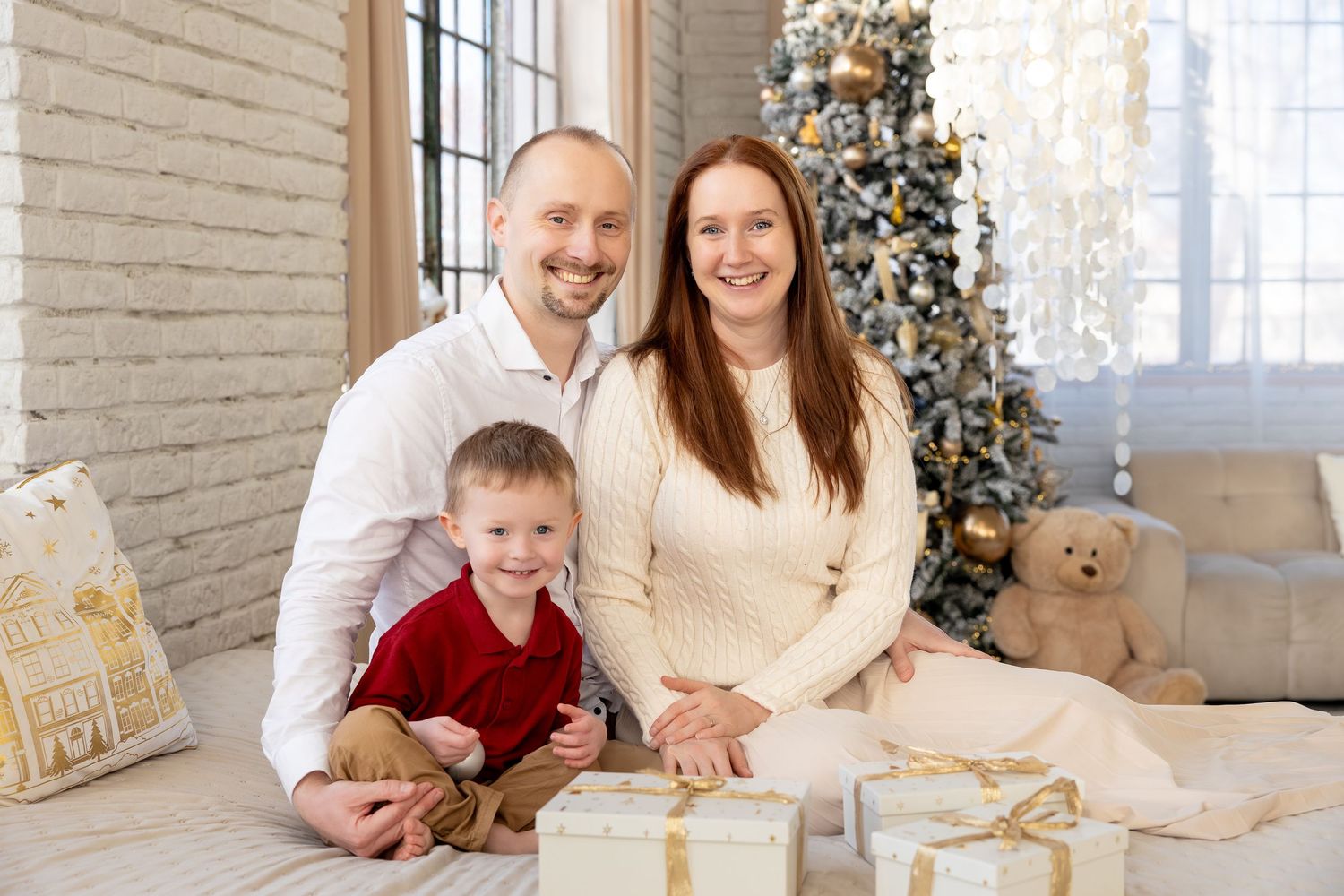 A family sits together on a white couch near a decorated Christmas tree in a bright living room.