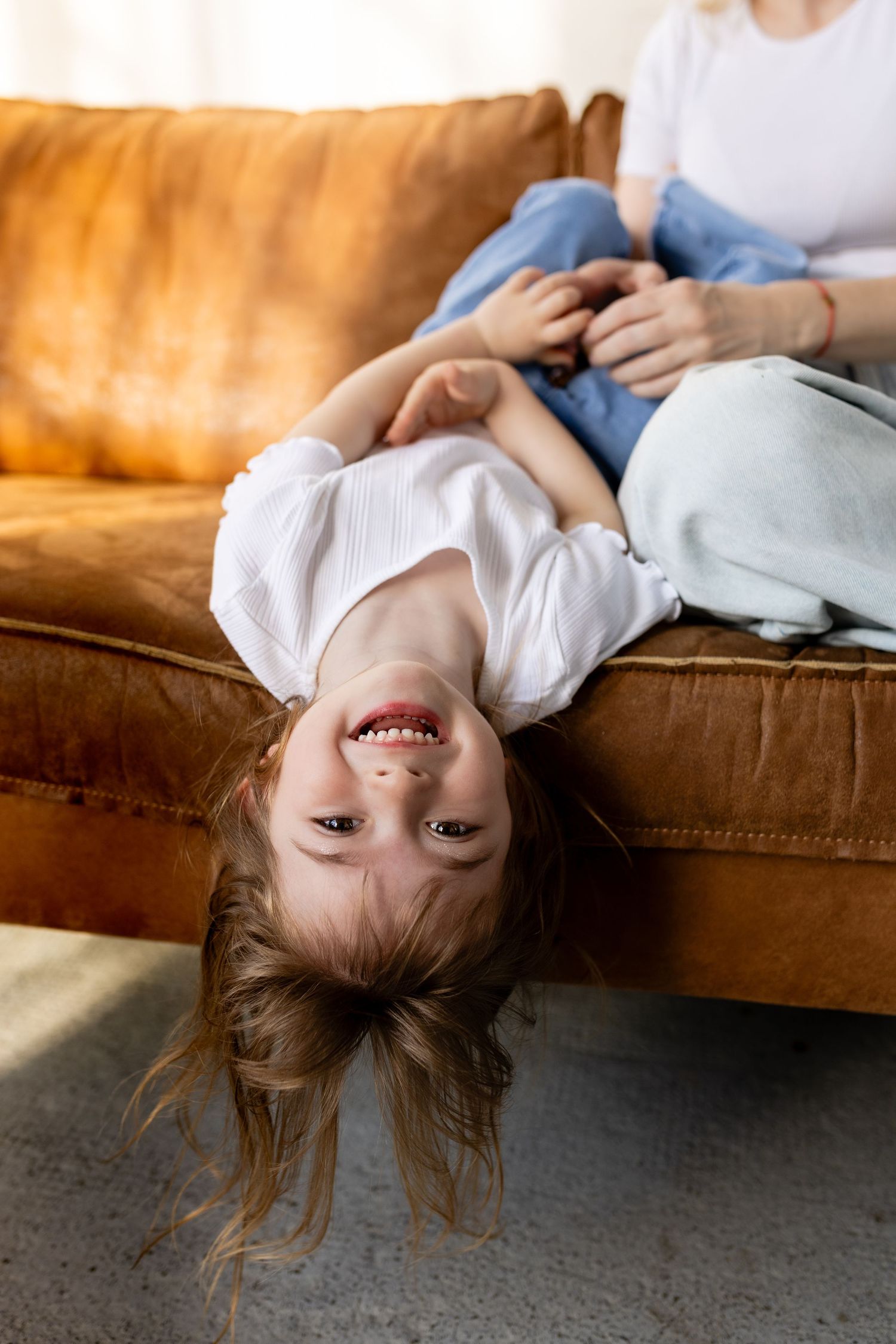 A person lies upside down on a brown leather couch with hair hanging down, showing a playful and carefree moment.