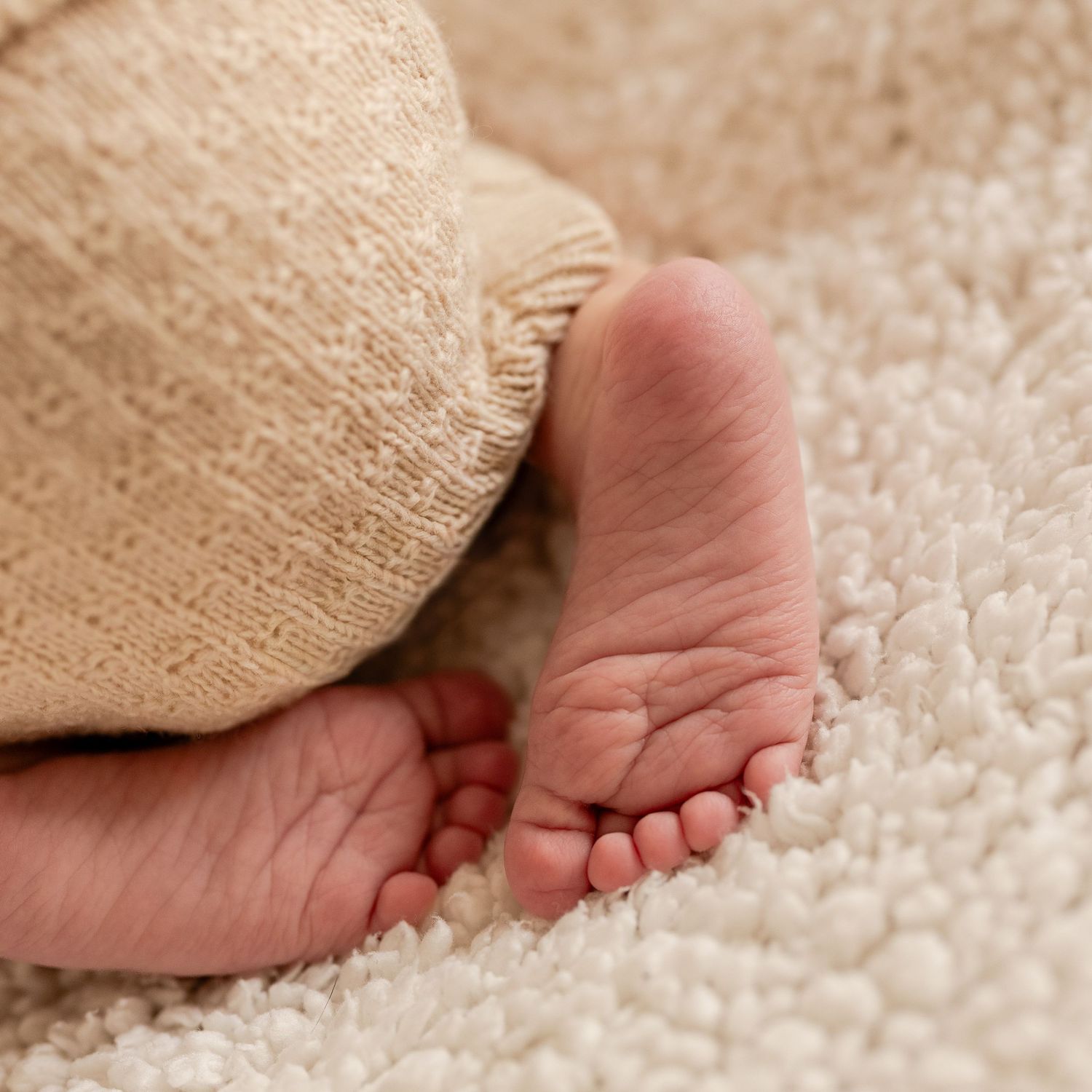 Close-up of newborn baby feet resting on a soft cream carpet, wrapped in a cozy knit blanket.
