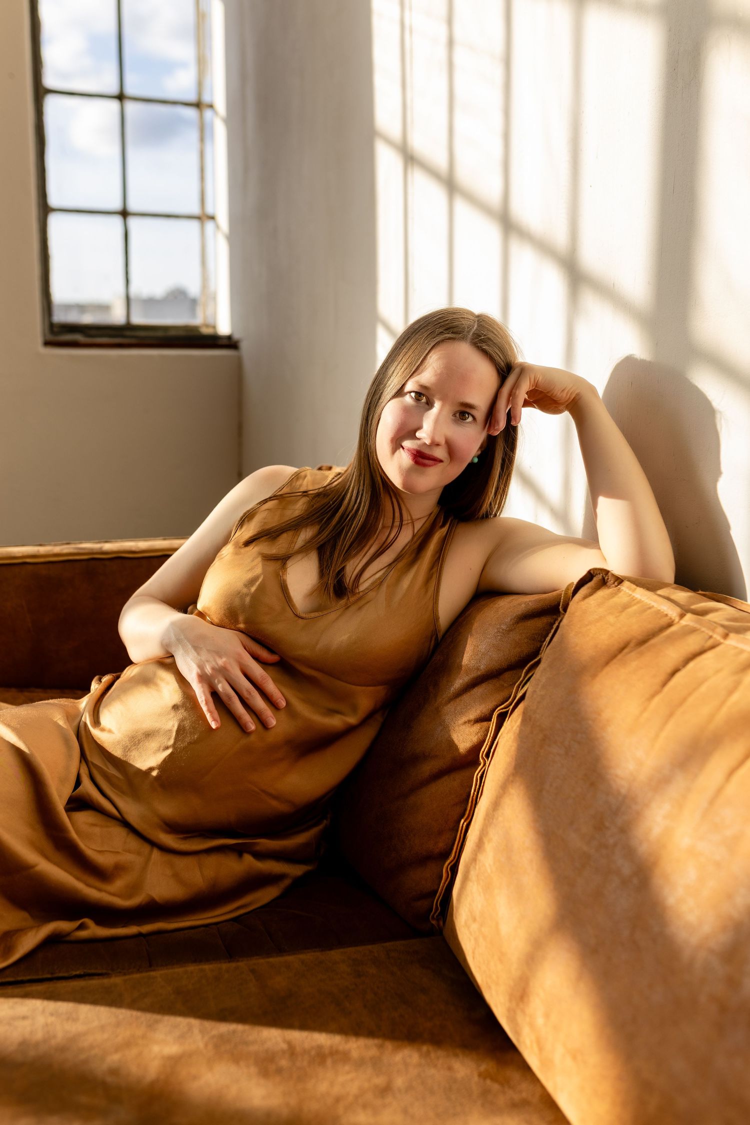Person relaxes on a brown leather couch in warm sunlight streaming through windows creating dramatic shadows.